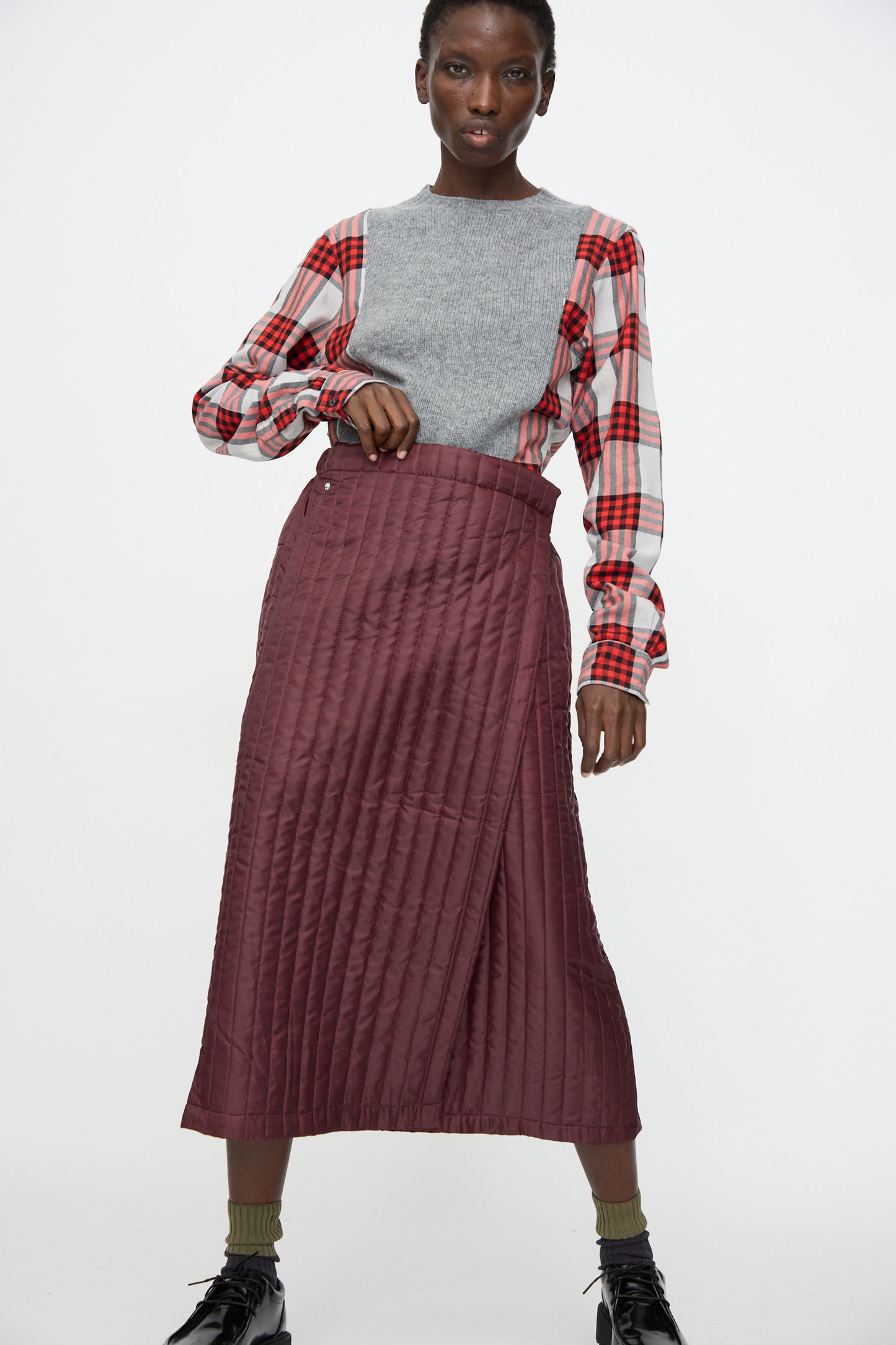 A person wearing a gray sleeveless top over a red plaid shirt and the Bless No. 08 Monpe Skirt in Burgundy, standing against a plain white background.