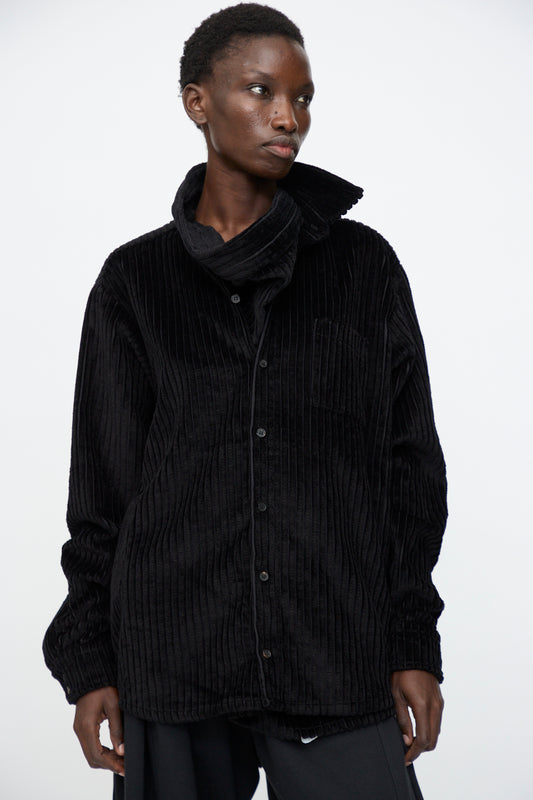 A person wears the Bless No. 68 Neckerchiefer in Black Corduroy—a high wrap-collar, button-up shirt—while standing against a plain white background.