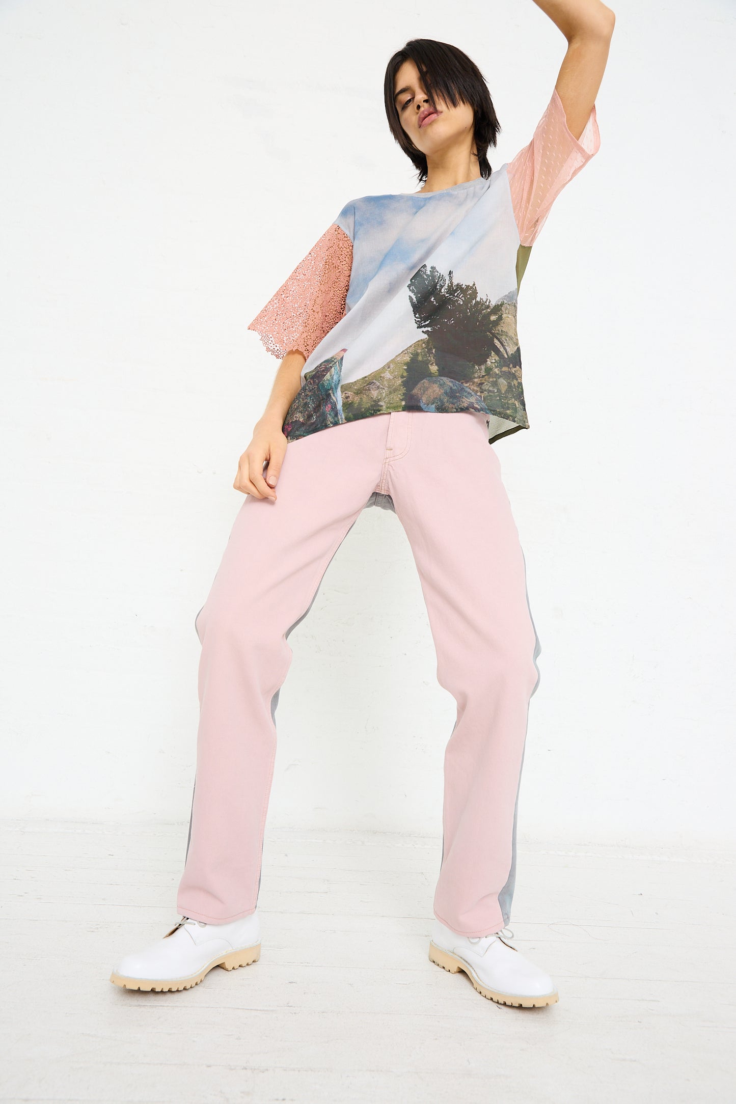 Woman in an up-cycled Bless vintage denim tee and No. 73 Jeanspleatfront trousers in Pink/Grey posing against a white background.