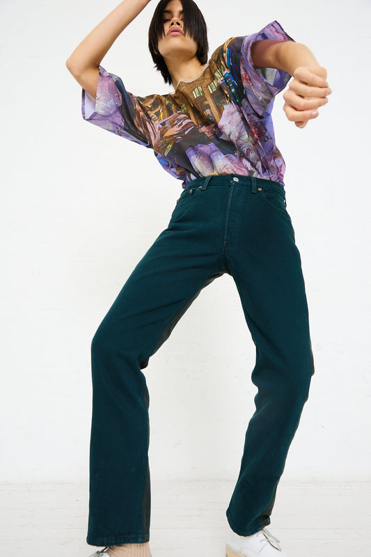Person posing dynamically in an up-cycled vintage denim Bless shirt and dark green trousers.