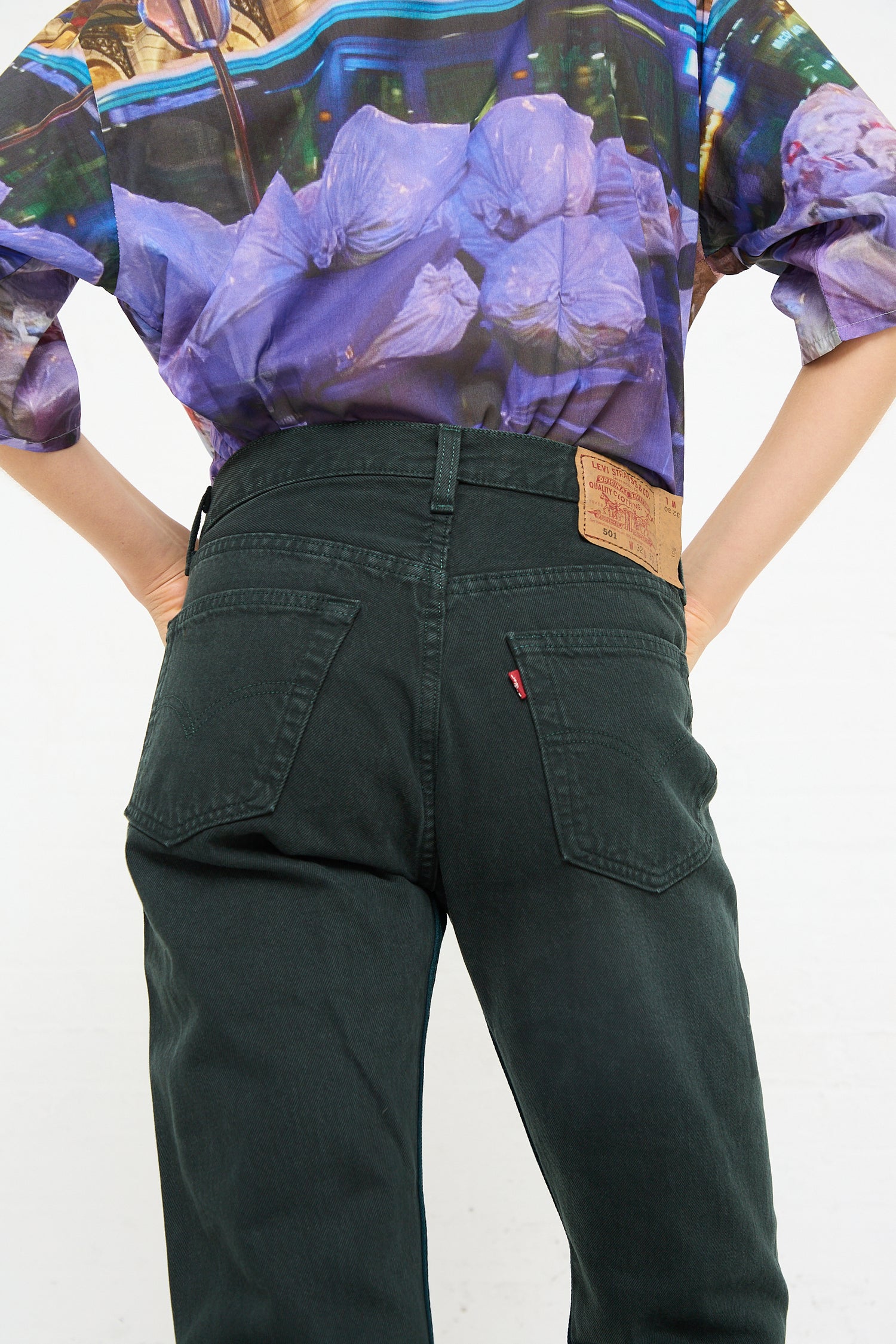 Person wearing green, Bless No. 73 Jeanspleatfront in Dark Teal/Grey and a floral print shirt from the waist to mid-back view.