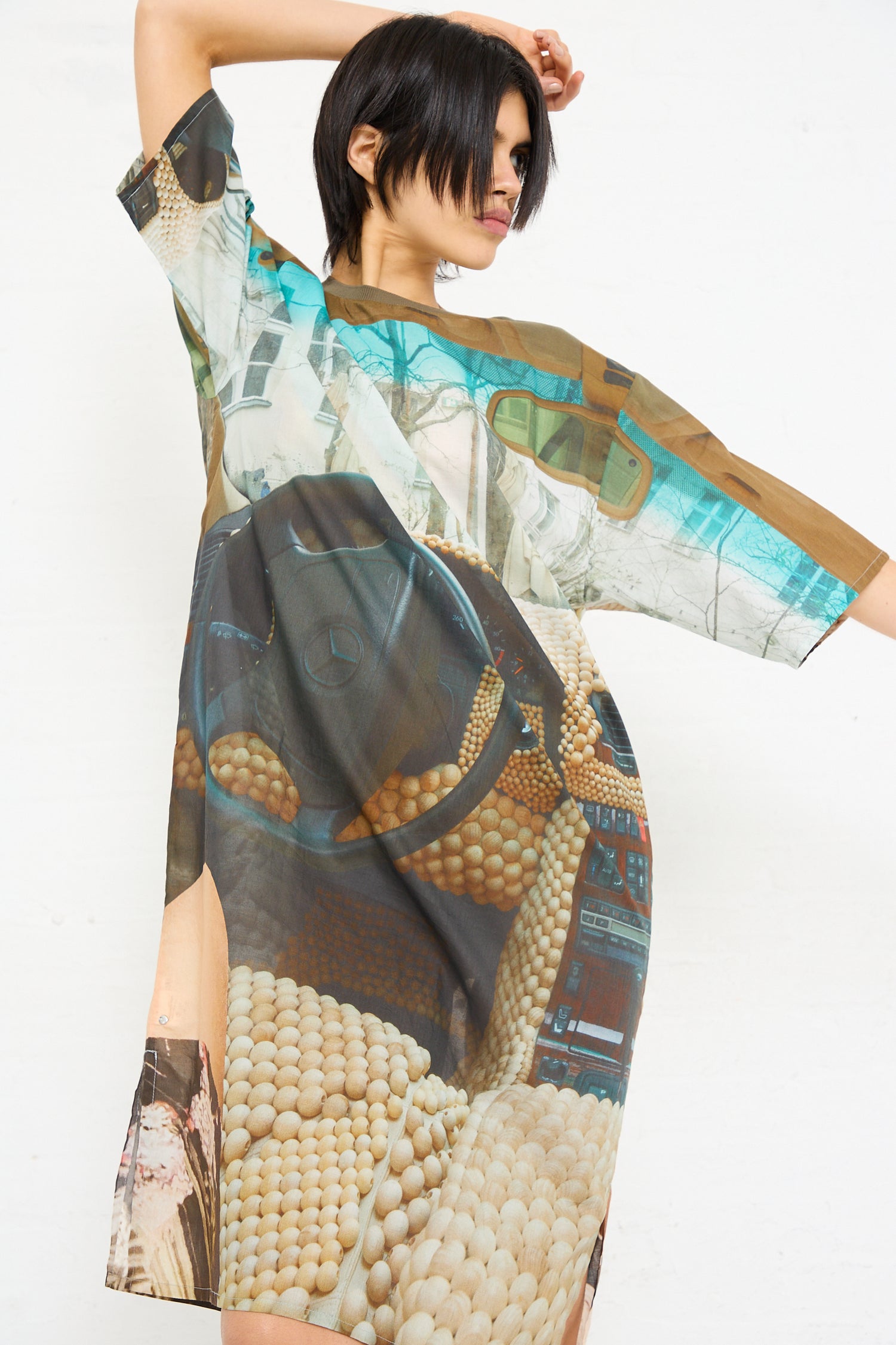 A woman posing in an oversized Bless No. 77 Sauna Rider Holiday Dress in Print with a collage-like graphic print against a white background.