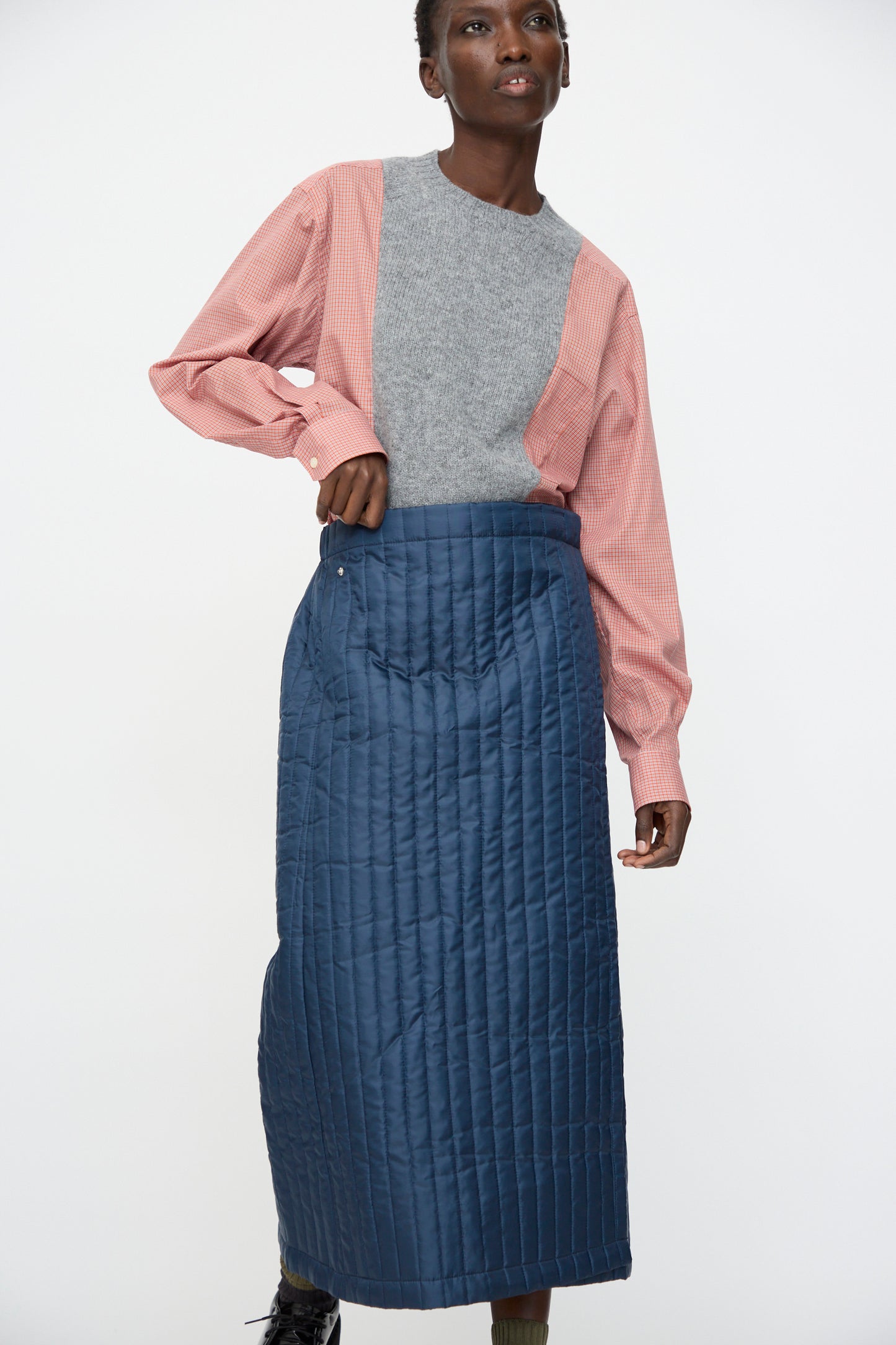A person in a red checkered shirt, gray sweater vest, and the Bless No. 08 Monpe Skirt in Navy with an adjustable snap waist stands against a plain white background.