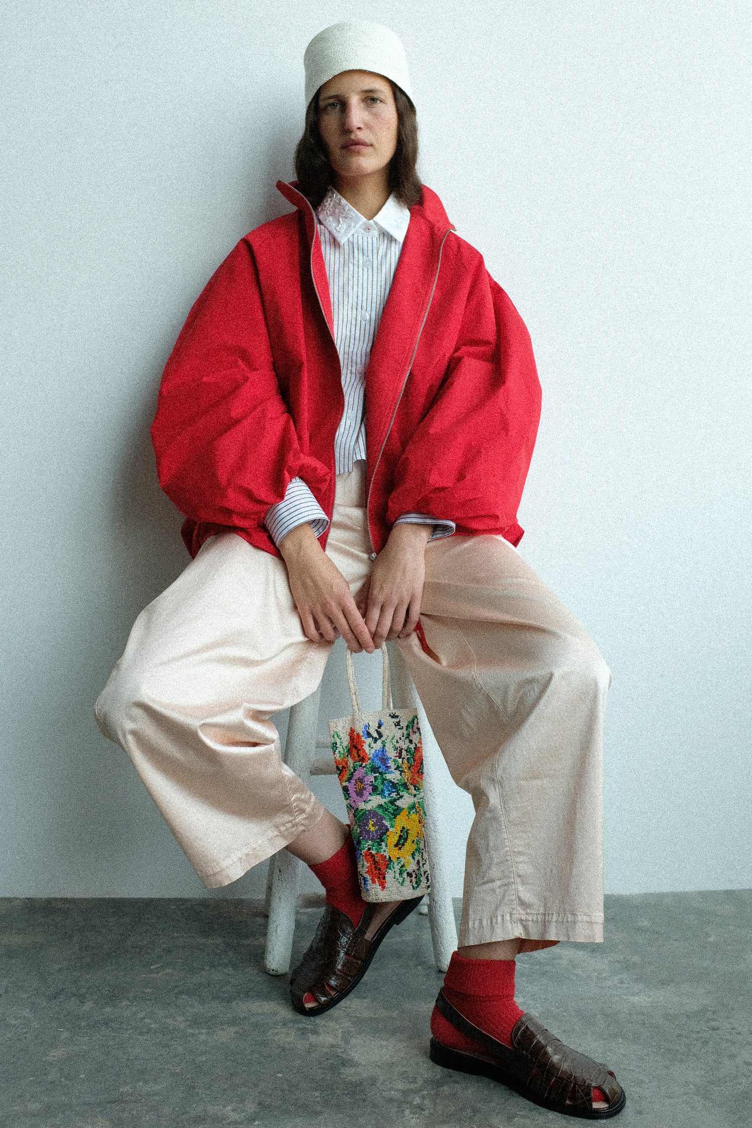 Person wearing a red coat and white pants sitting on a stool against a plain background
