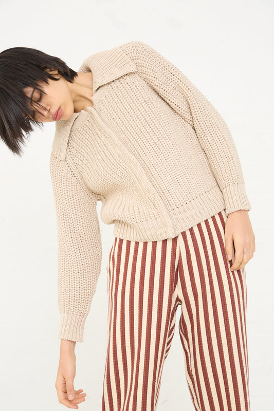 A person wearing a Caron Callahan Cotton and Alpaca Freda Cardigan in Ecru and striped trousers with one hand in their pocket.