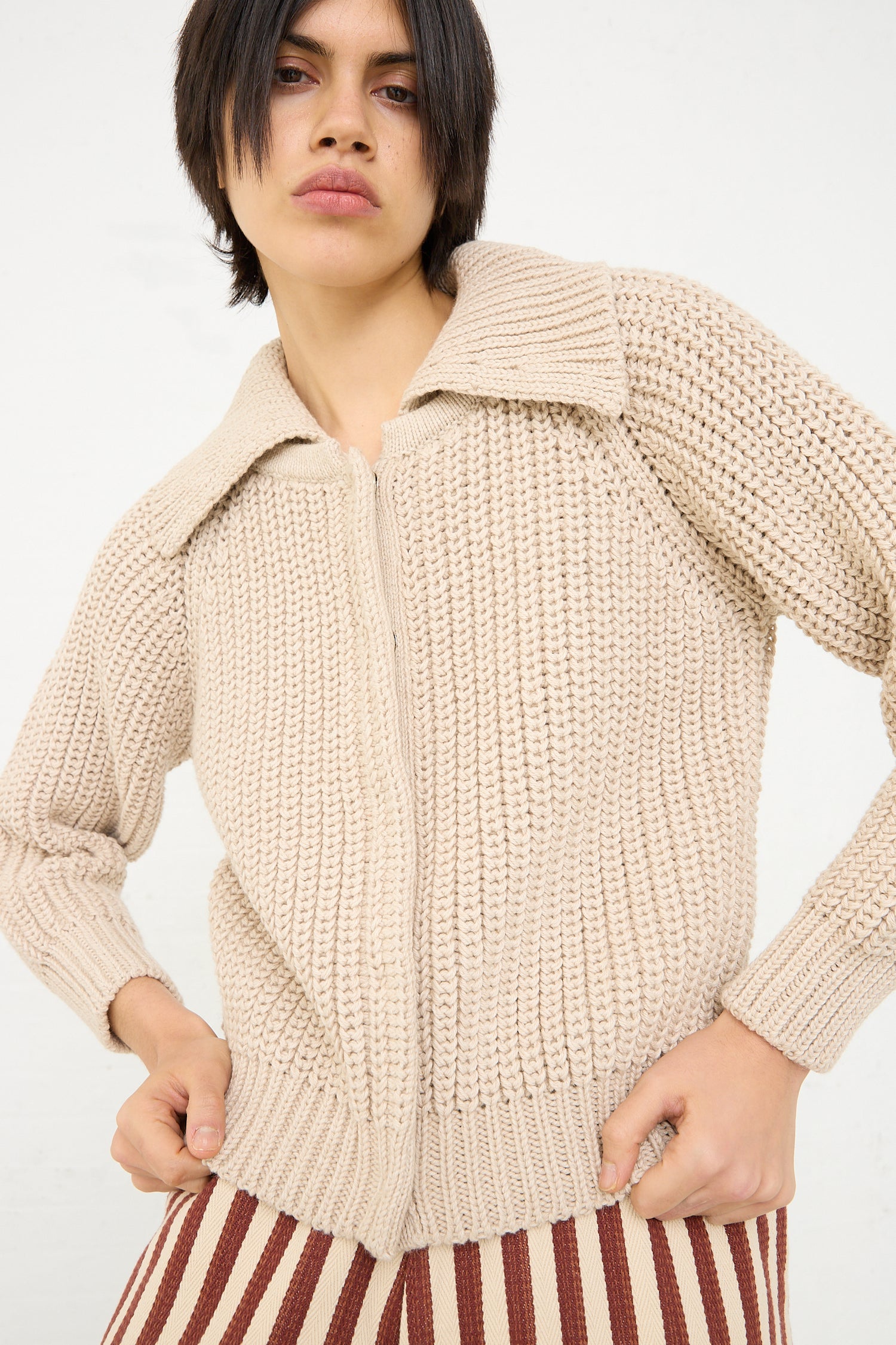 A person posing in a Cotton and Alpaca Freda Cardigan in Ecru by Caron Callahan with hands on hips against a white background.