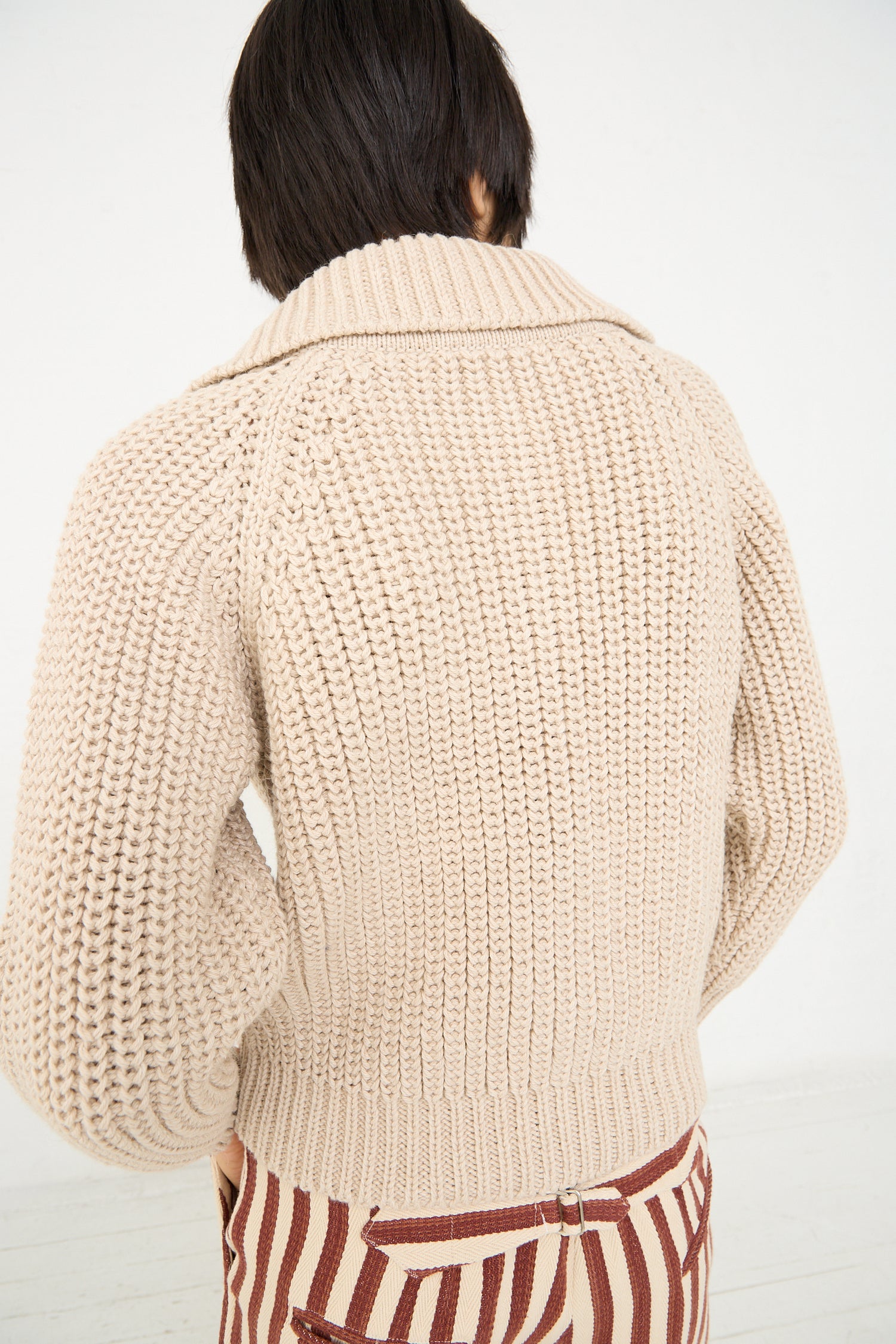 A person seen from behind wearing a Caron Callahan Cotton and Alpaca Freda Cardigan in Ecru and striped pants.