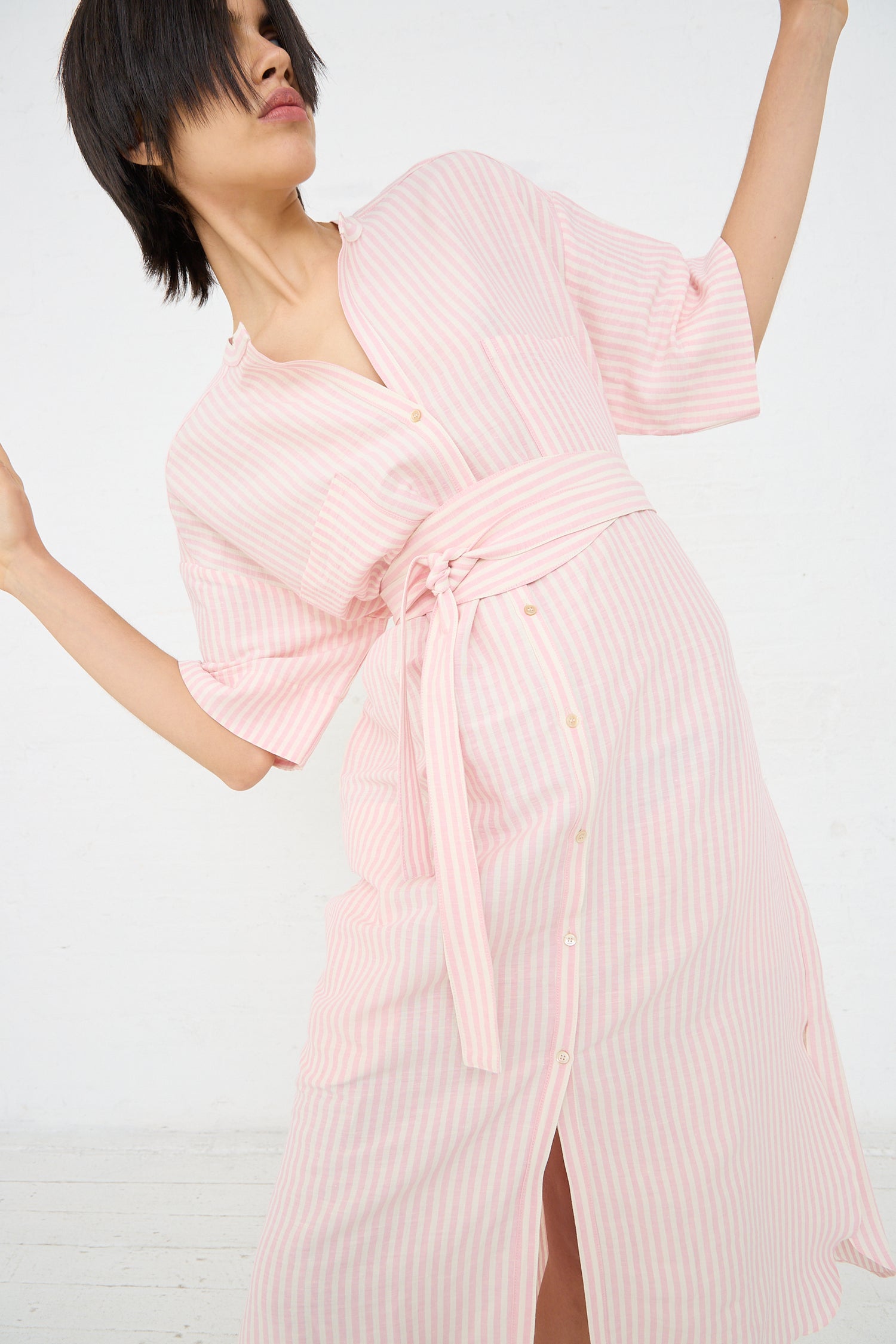 Woman posing in a Linen Stripe Kalloni Dress in Pink by Caron Callahan, an oversized shirt dress with a striped pink and white linen blend fabric and a knotted waist detail.