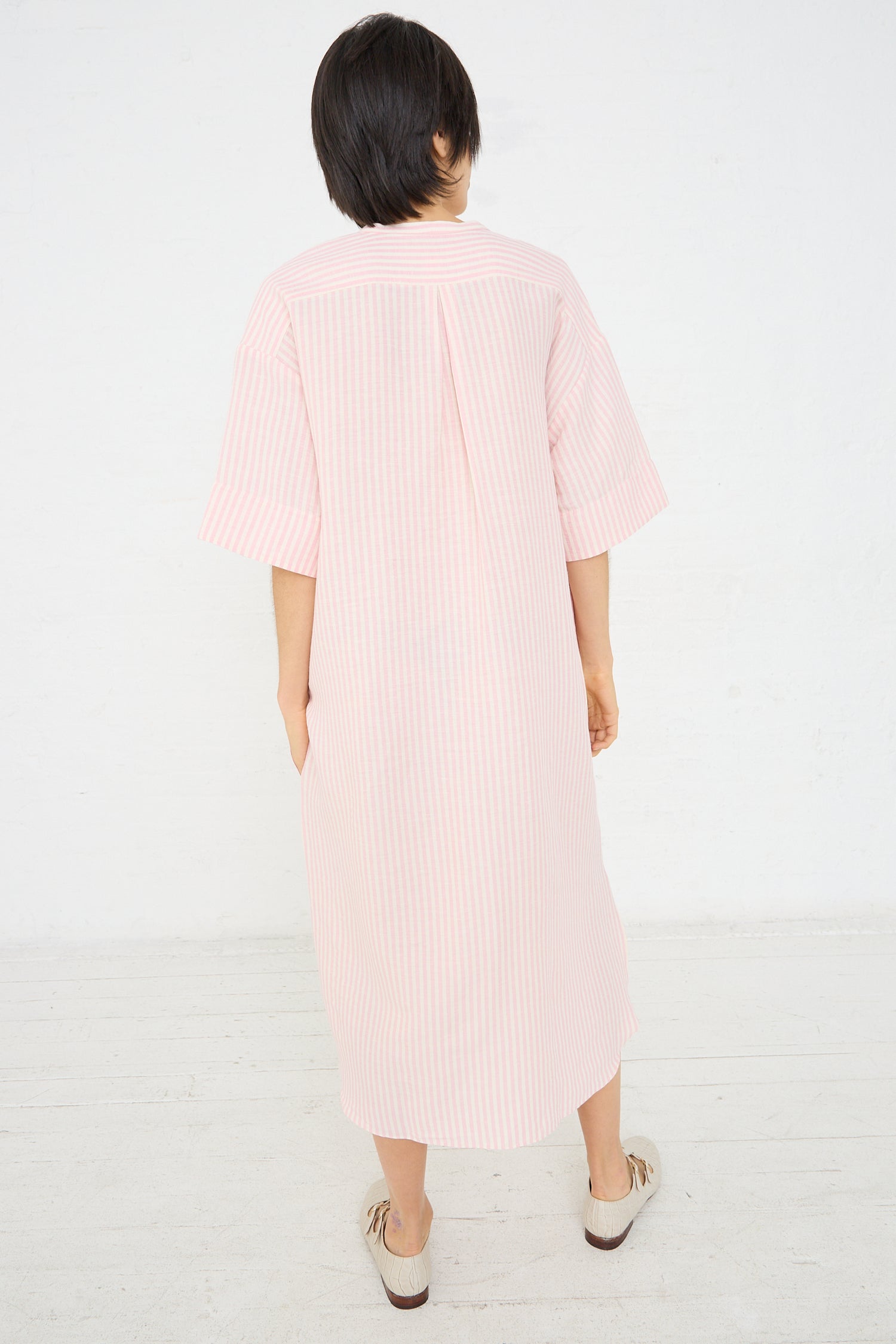 A person from behind wearing a Caron Callahan Linen Stripe Kalloni Dress in Pink with mid-length sleeves, standing in front of a white background.