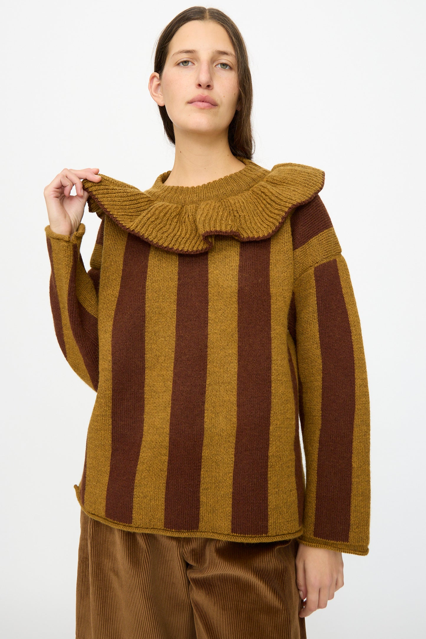 A woman wears the Cawley British Merino Wool Striped Ruffle Jumper in Goldfinch and Bordeaux, featuring a boxy fit and ruffled collar, paired with brown corduroy pants against a plain white background.