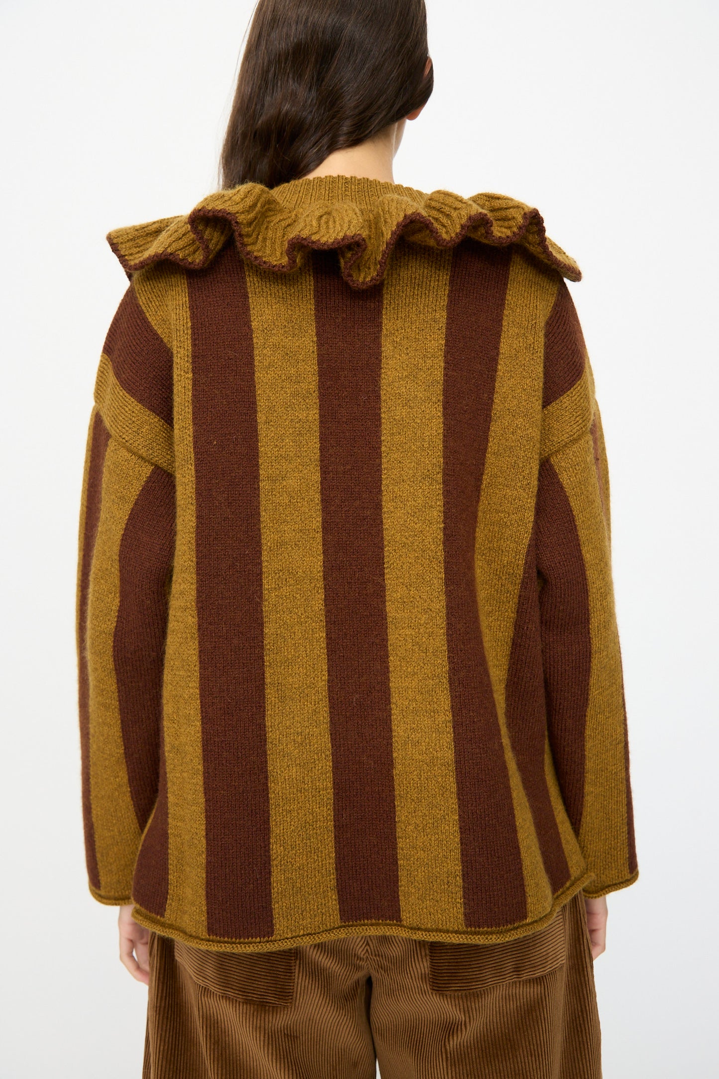 A person is seen from the back wearing the Cawley British Merino Wool Striped Ruffle Jumper in Goldfinch and Bordeaux, featuring a boxy fit with vertical stripes and a ruffled collar.