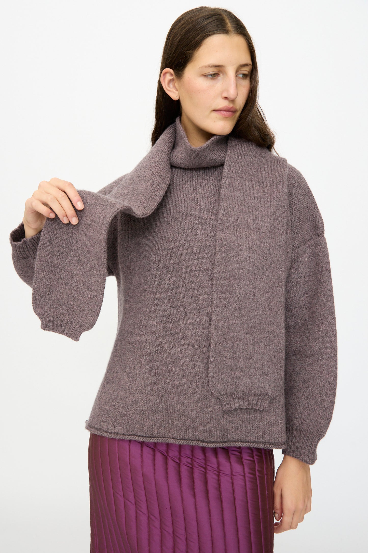 A woman wears the Cawley British Merino Wool Wrap Neck Pullover in Luna, paired with a matching scarf and purple pleated skirt, standing against a plain white background.