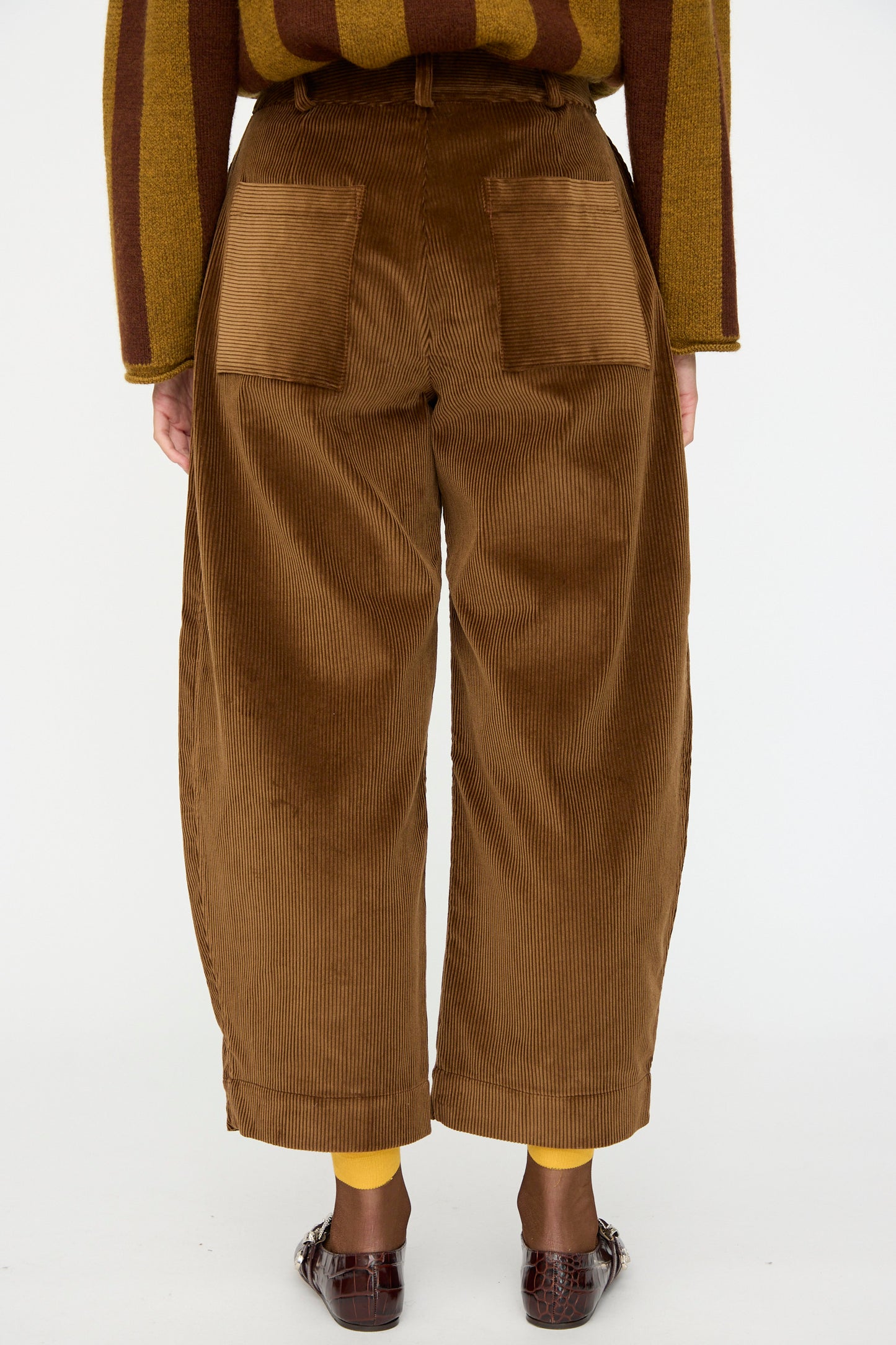 A person is shown from the back wearing Cawley's Cotton Wale Cord Robyn Trouser in Tan, paired with yellow socks, brown shoes, and a brown and yellow striped sweater.