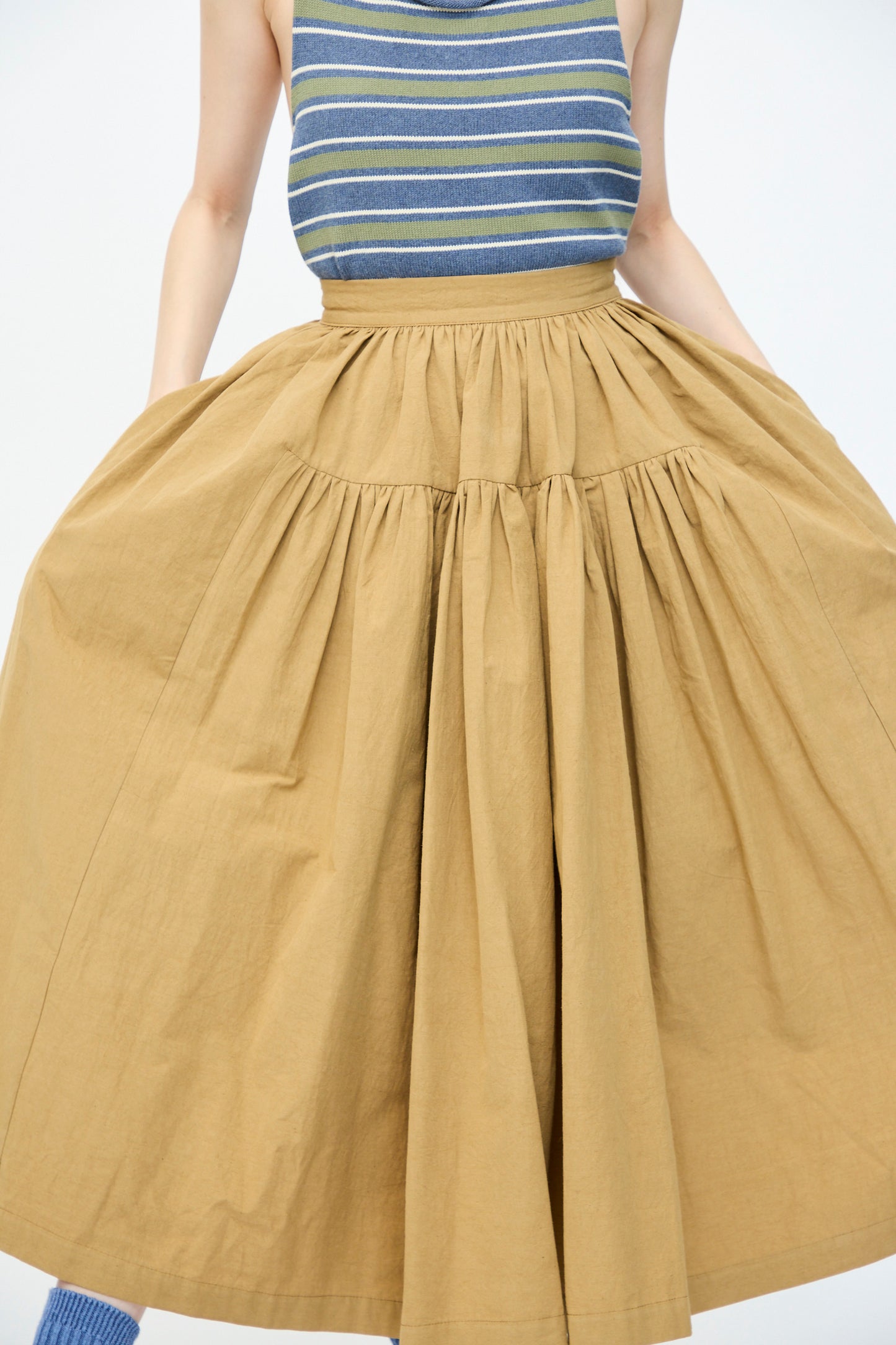 A person in a striped sleeveless top and Cawley's Japanese Paper Cotton Panel Skirt in Nutmeg poses against a plain background.