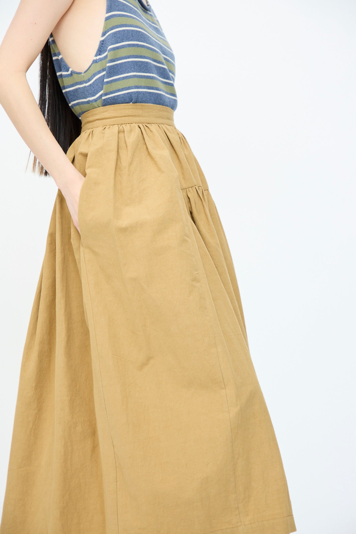 A person wearing Cawley's Japanese Paper Cotton Panel Skirt in Nutmeg, featuring a flattering A-line silhouette, stands with hands in pockets against a plain white background.