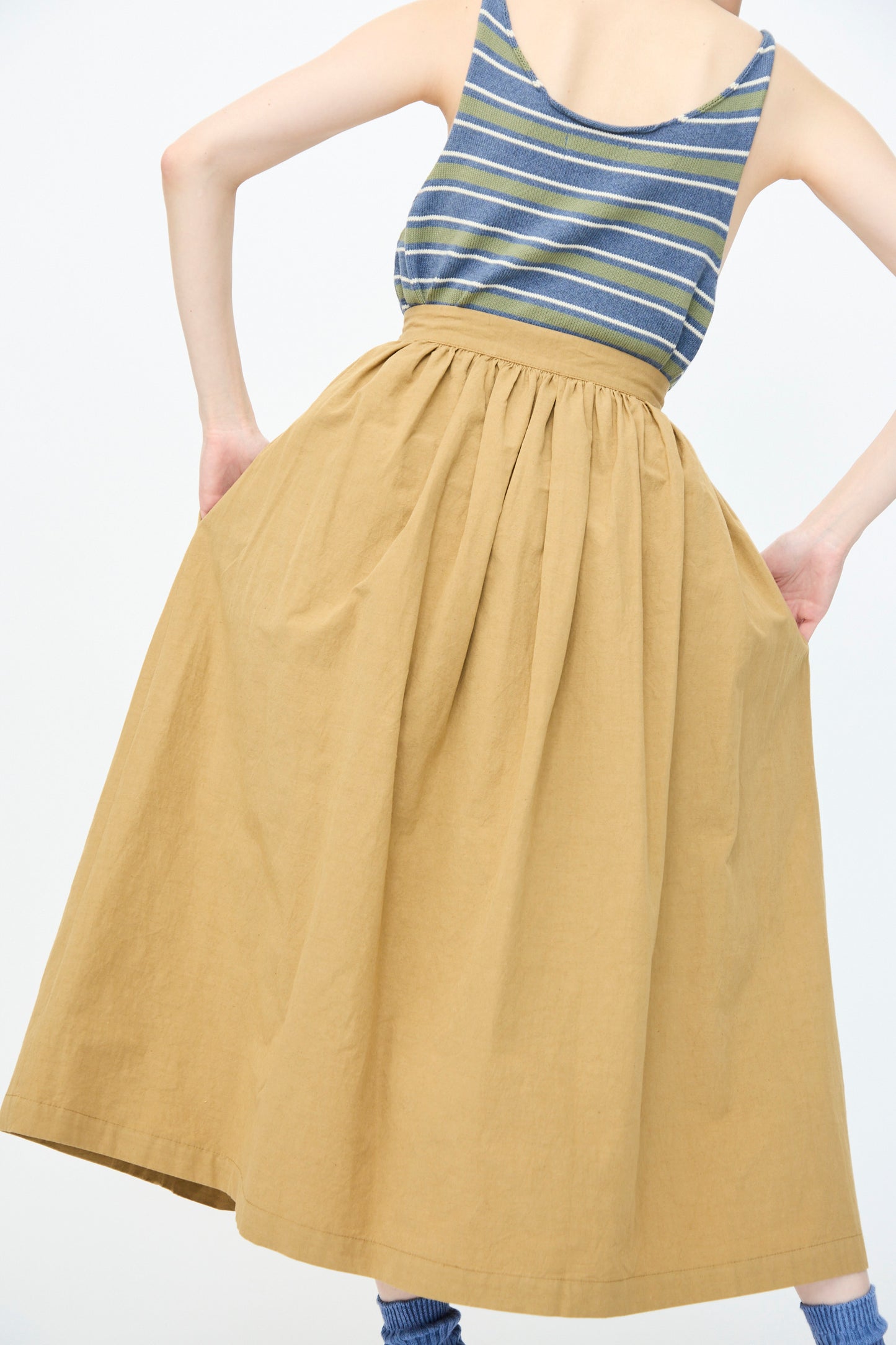 A person is photographed from the back wearing a sleeveless striped top with Cawley's Japanese Paper Cotton Panel Skirt in Nutmeg, high-waisted and knee-length, against a plain background.