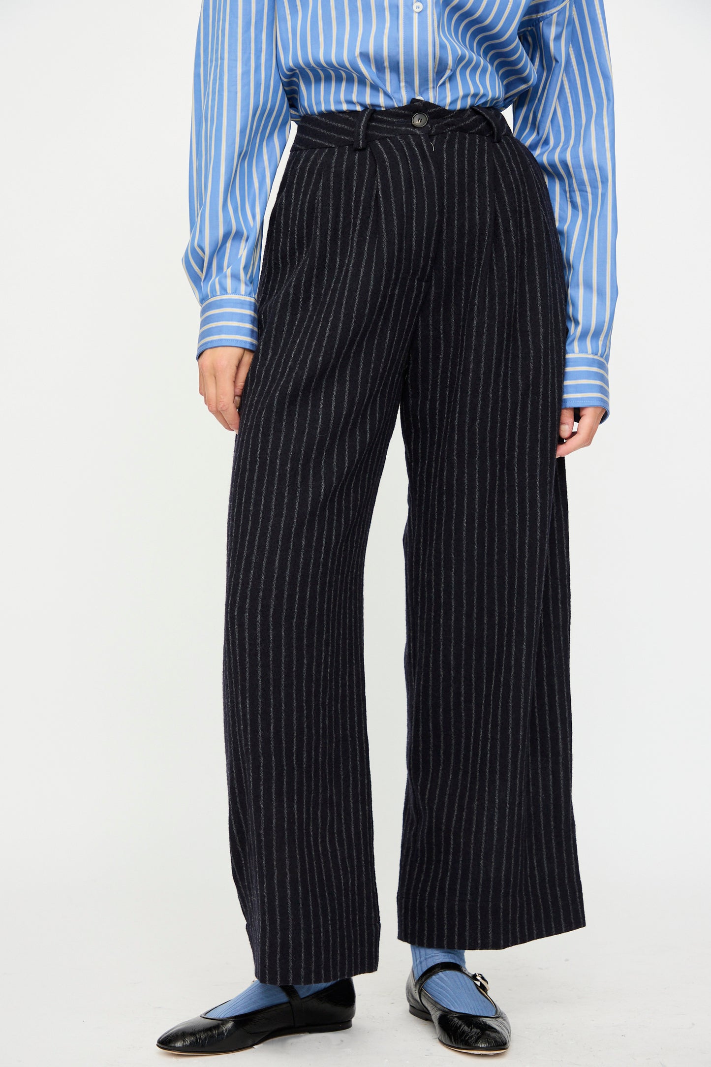 Person wearing a blue and white striped shirt, Cawley Japanese Striped Boucle Mara Trouser in Navy and Grey, blue socks, and black shoes, standing against a plain background.