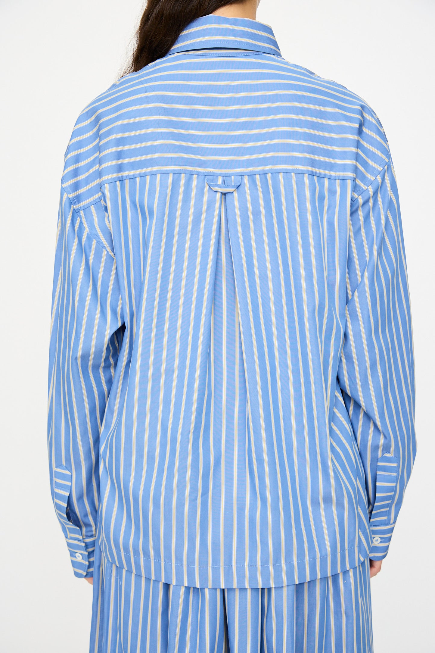 A person is shown from the back wearing the Cawley Japanese Striped Dennis Shirt in Blue Dandelion Stripe, with long hair visible over one shoulder.