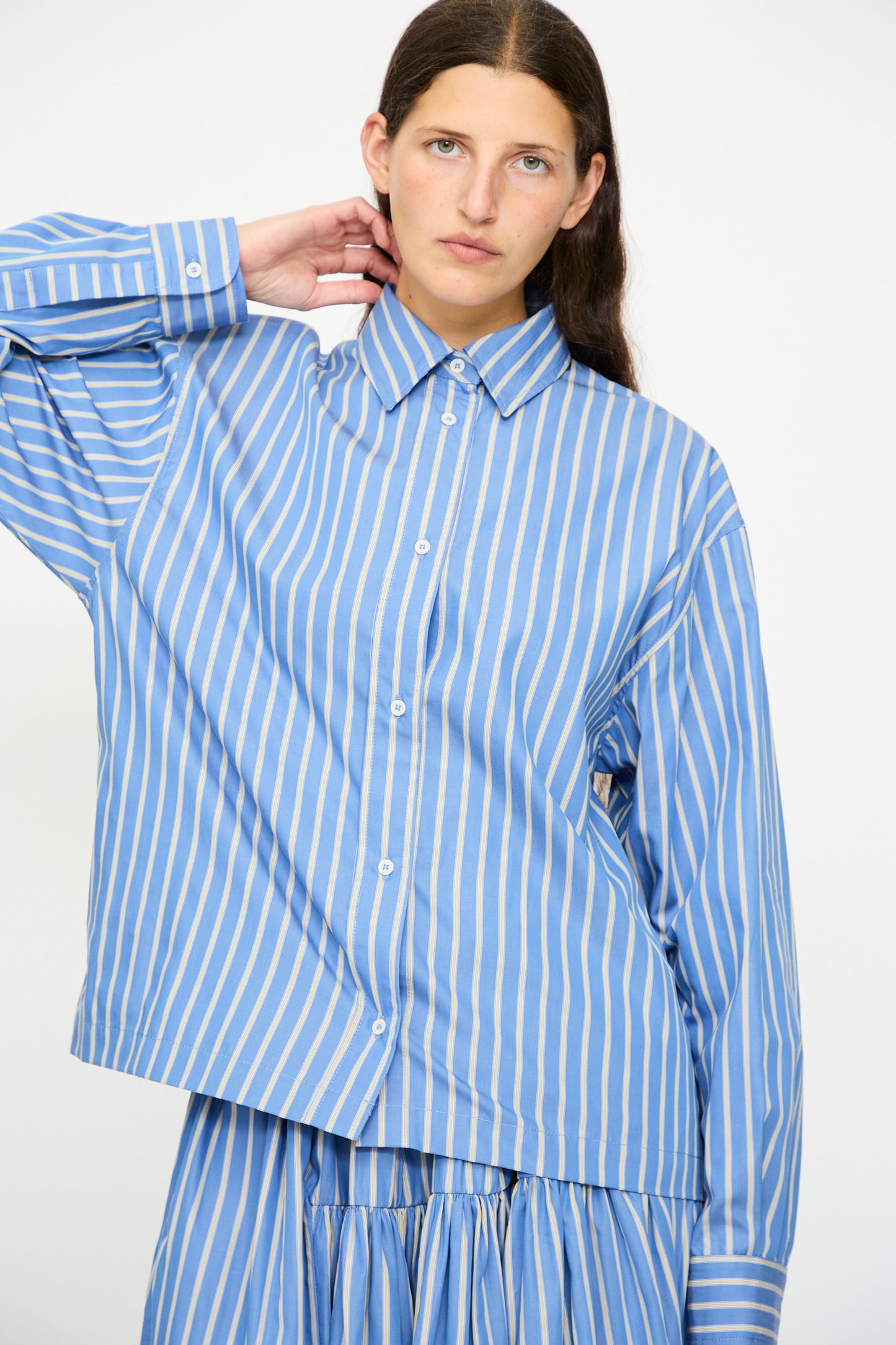 A person with long brown hair wears the Cawley Japanese Striped Dennis Shirt in Blue Dandelion Stripe, standing against a plain light background.