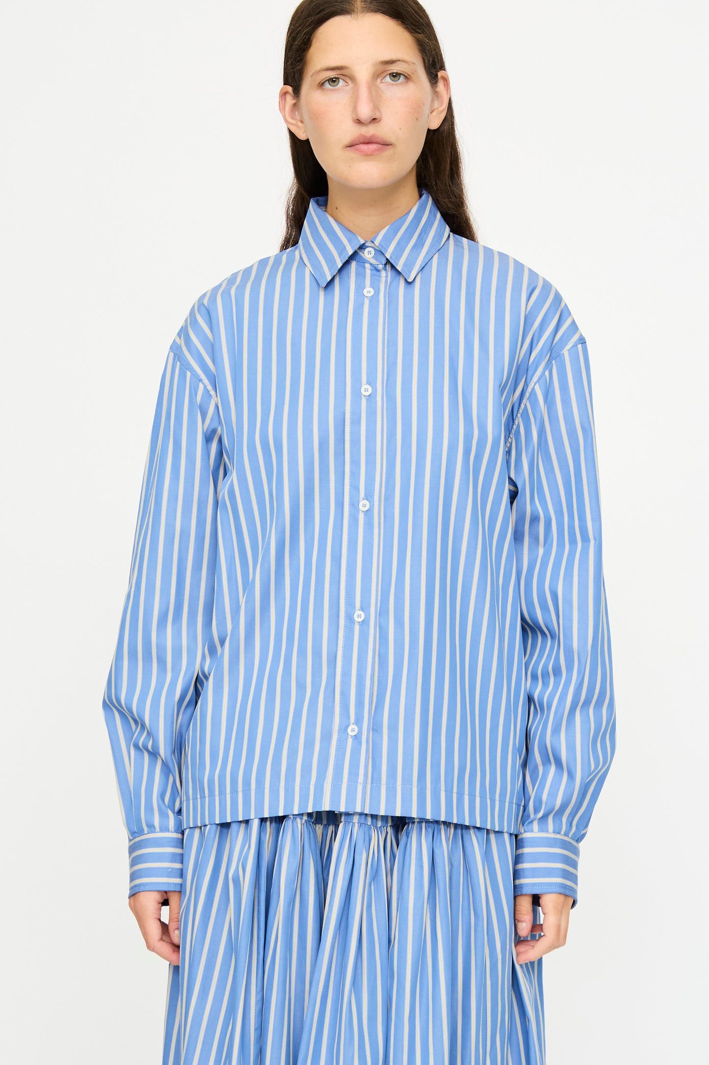 A person wears the Cawley Japanese Striped Dennis Shirt in Blue Dandelion Stripe paired with a matching skirt, standing against a plain white background.