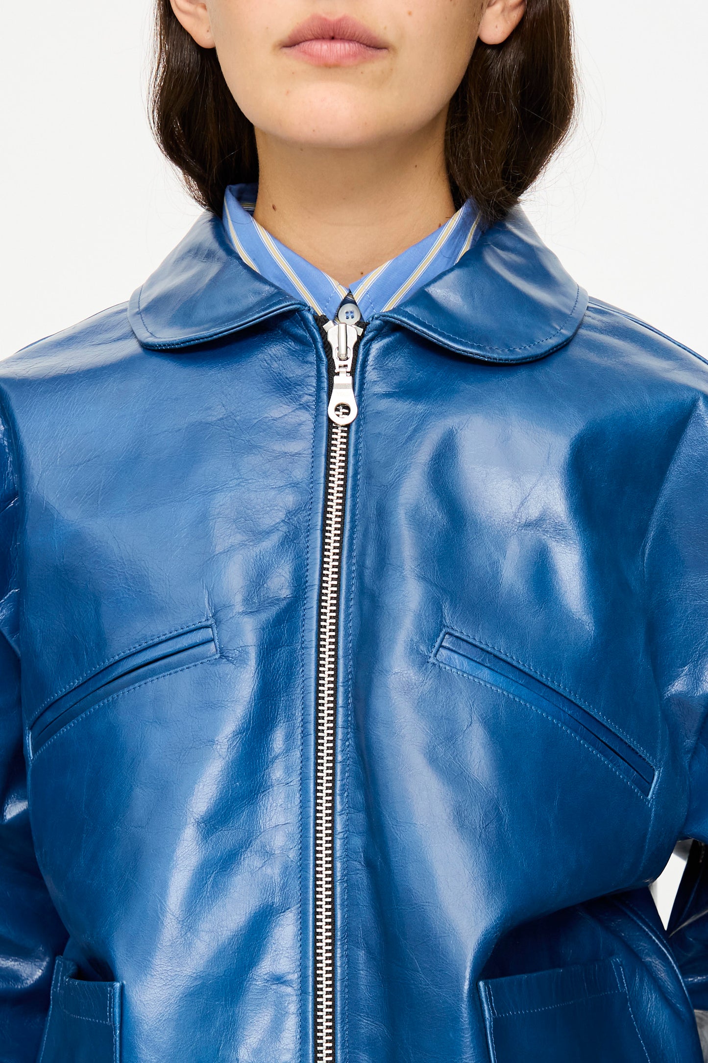 A person wearing the Cawley Leather Flying Jacket in Canada Blue, styled with an oversized fit over a blue collared shirt, photographed from shoulders to mouth.