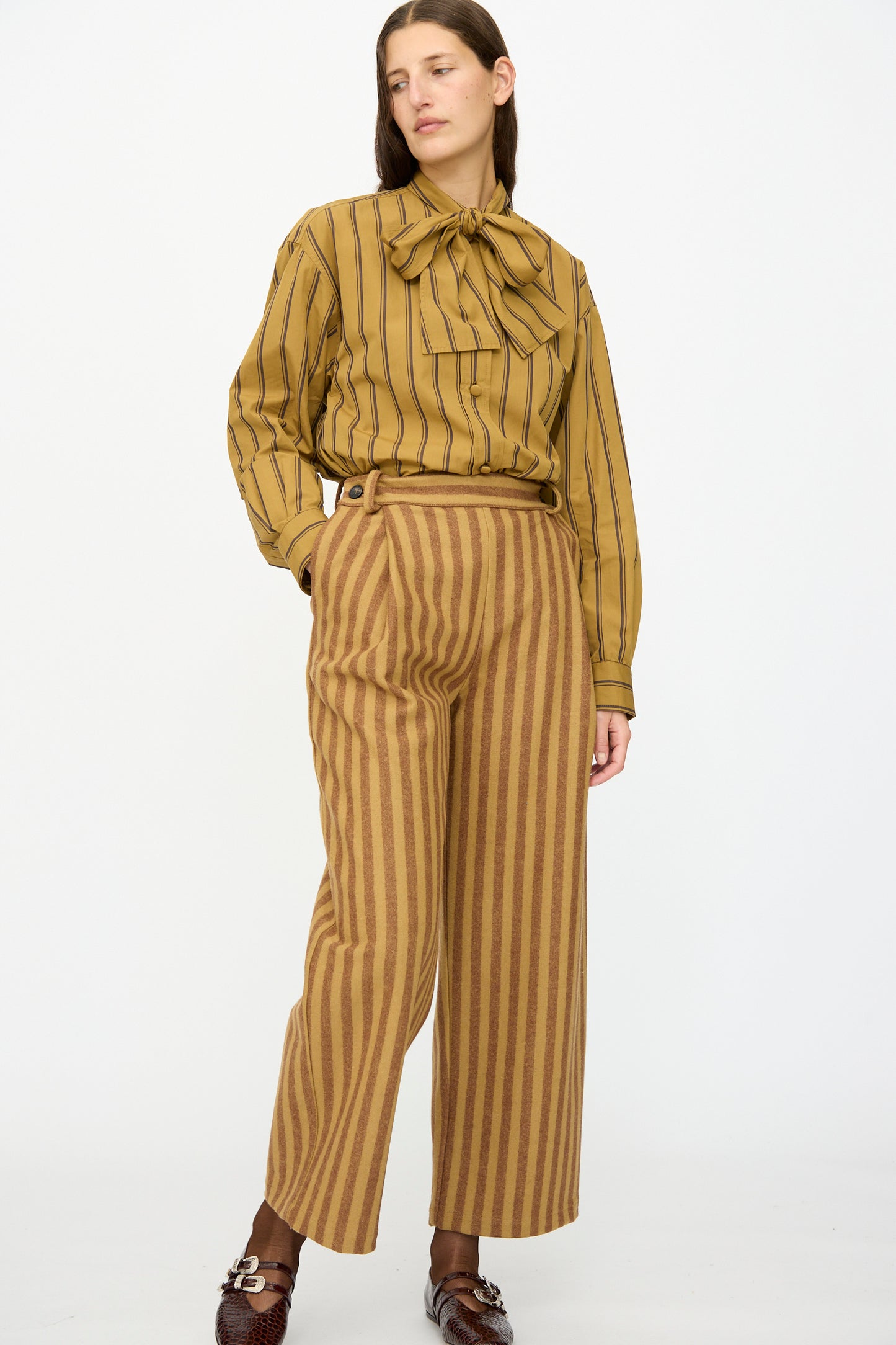 A woman stands against a plain background wearing Cawley's Portuguese Striped Wool Georgia Trouser in Goldfinch and Bordeaux.
