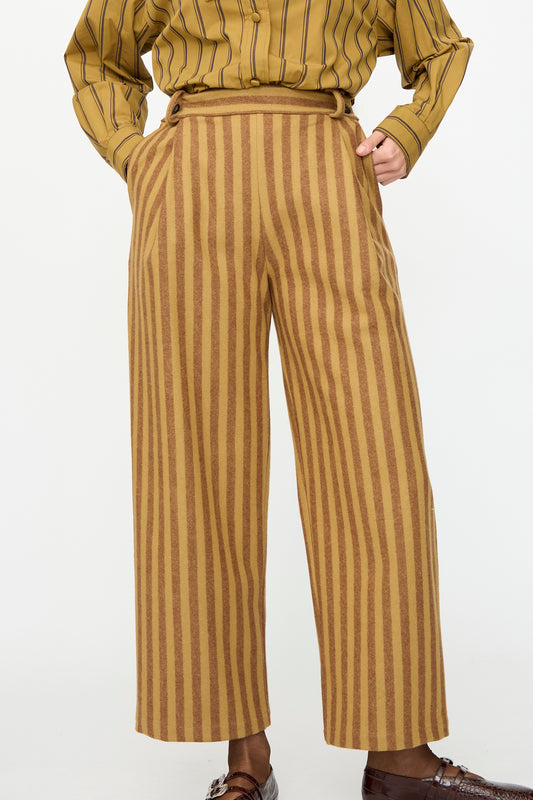 A person wears Cawley’s Portuguese Striped Wool Georgia Trouser in Goldfinch and Bordeaux with a mustard shirt and brown loafers. Only torso and legs are shown. Made in London.