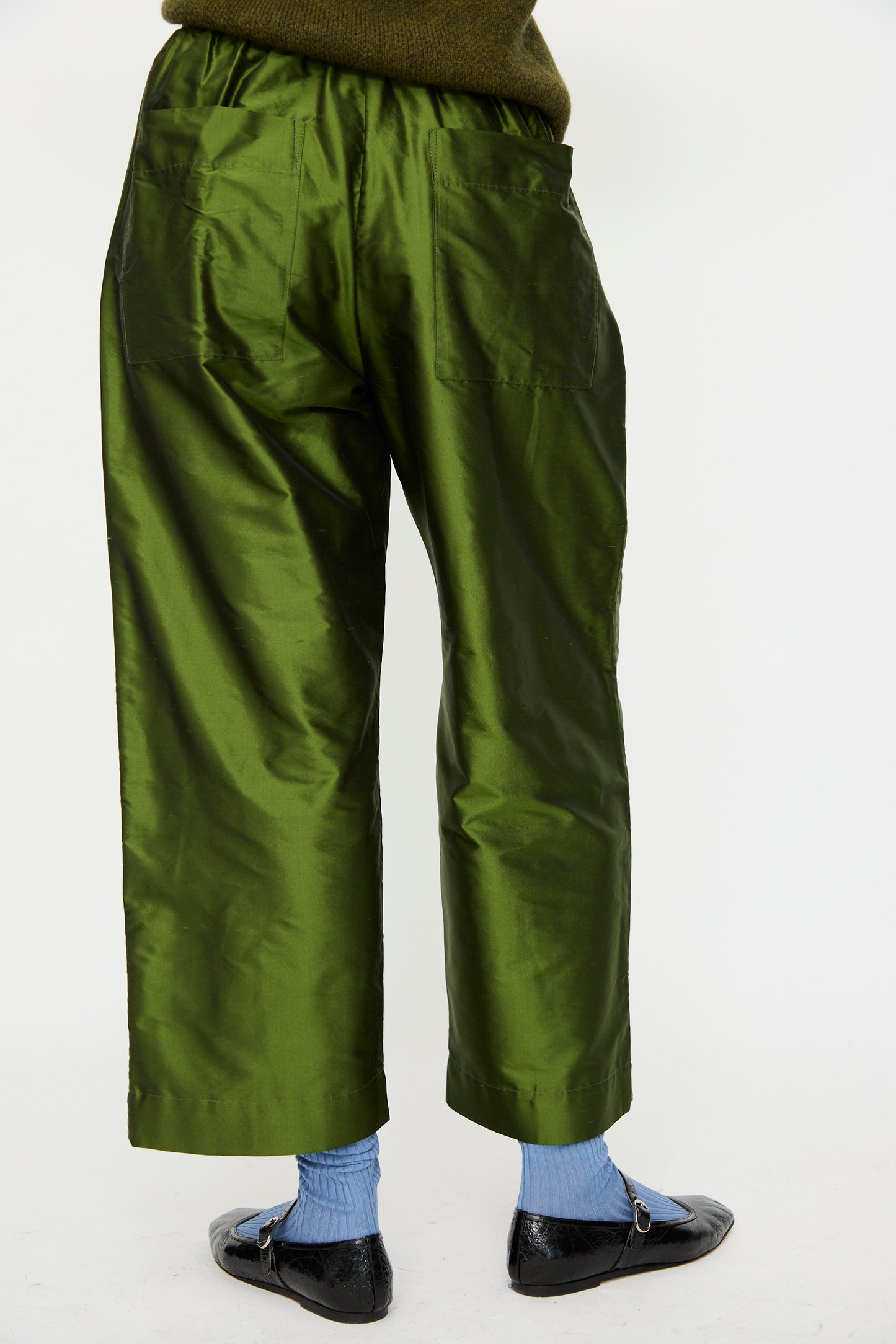 Person shown from the back wearing Cawley’s Silk Dupion Luna Trouser with Trim in Bottle, styled with light blue socks and black shoes, photographed against a plain white background. Trousers are crafted in London from luxurious silk dupion.