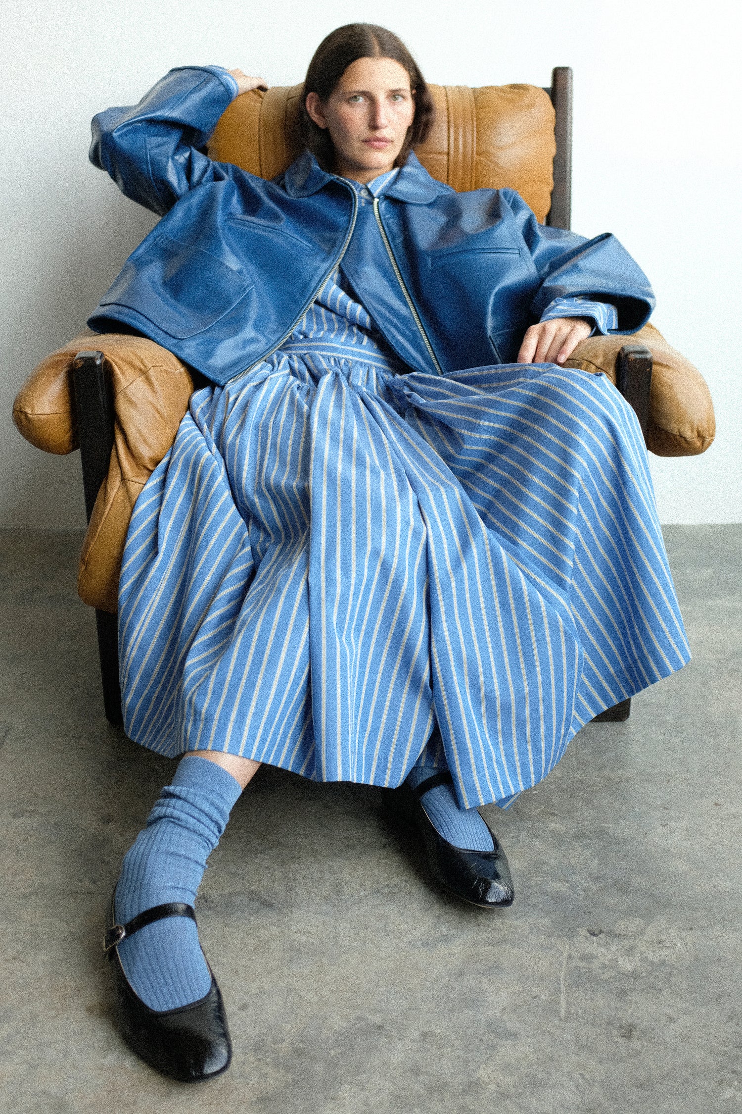 Woman sitting in a chair wearing a blue outfit with a striped dress and coat.