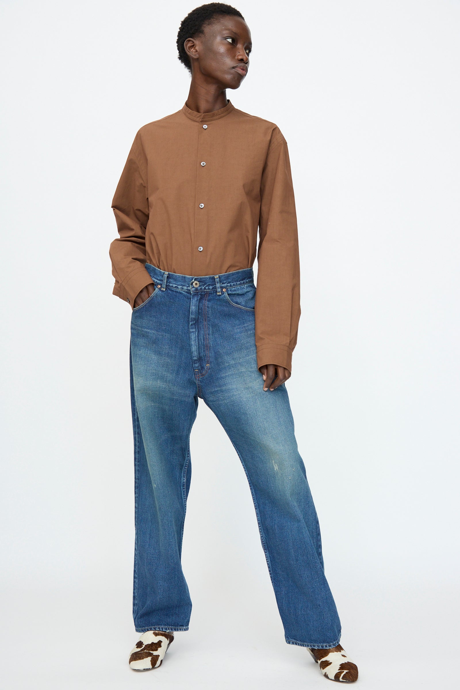 A person stands against a plain background, wearing a brown button-up shirt, patterned shoes, and Chimala 13oz. Selvedge Denim Ranch Pants in Dark Wash.