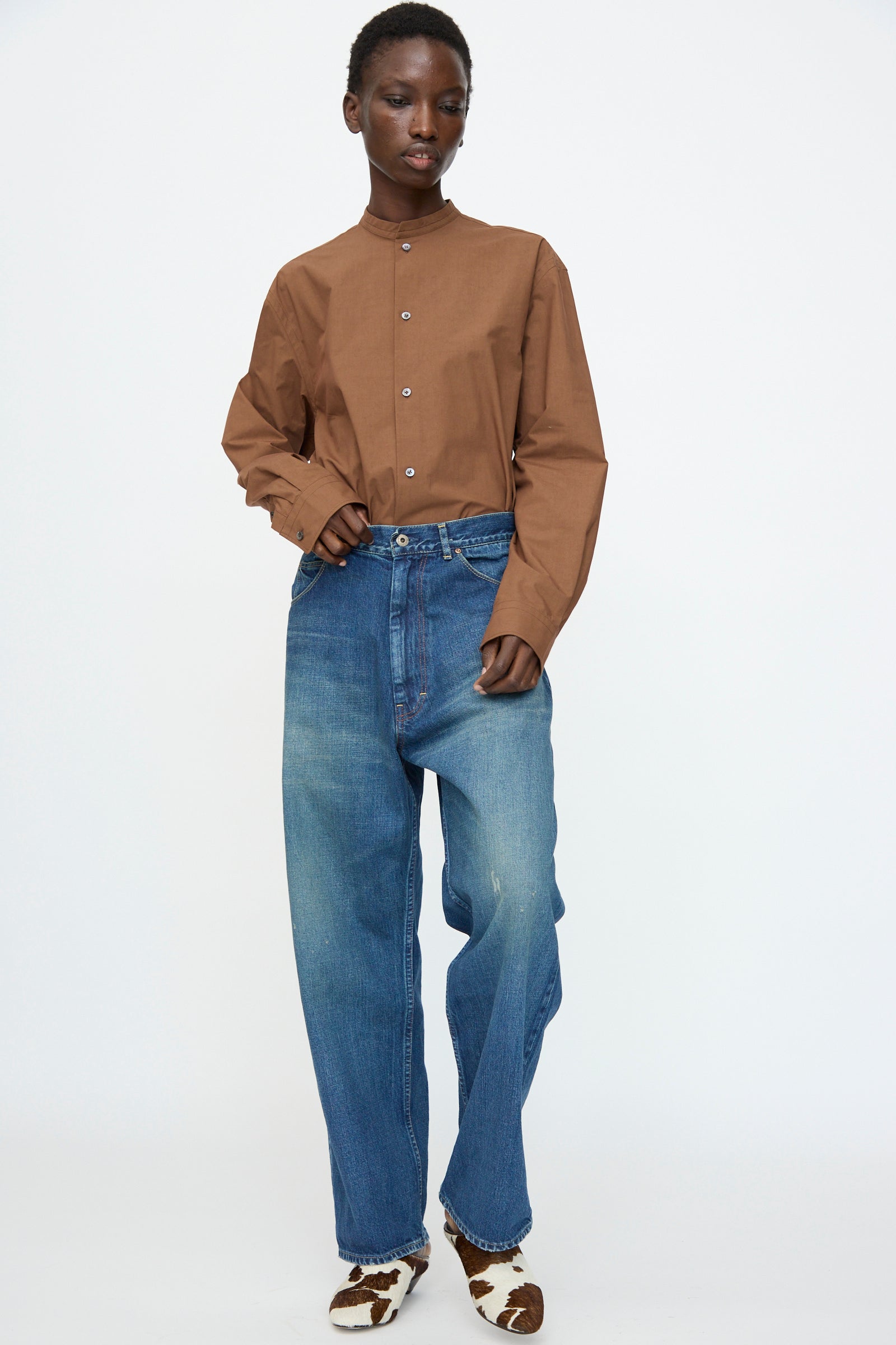 A person stands against a plain background wearing a brown button-up shirt, Chimala 13oz. Selvedge Denim Ranch Pants in Dark Wash, and patterned shoes.