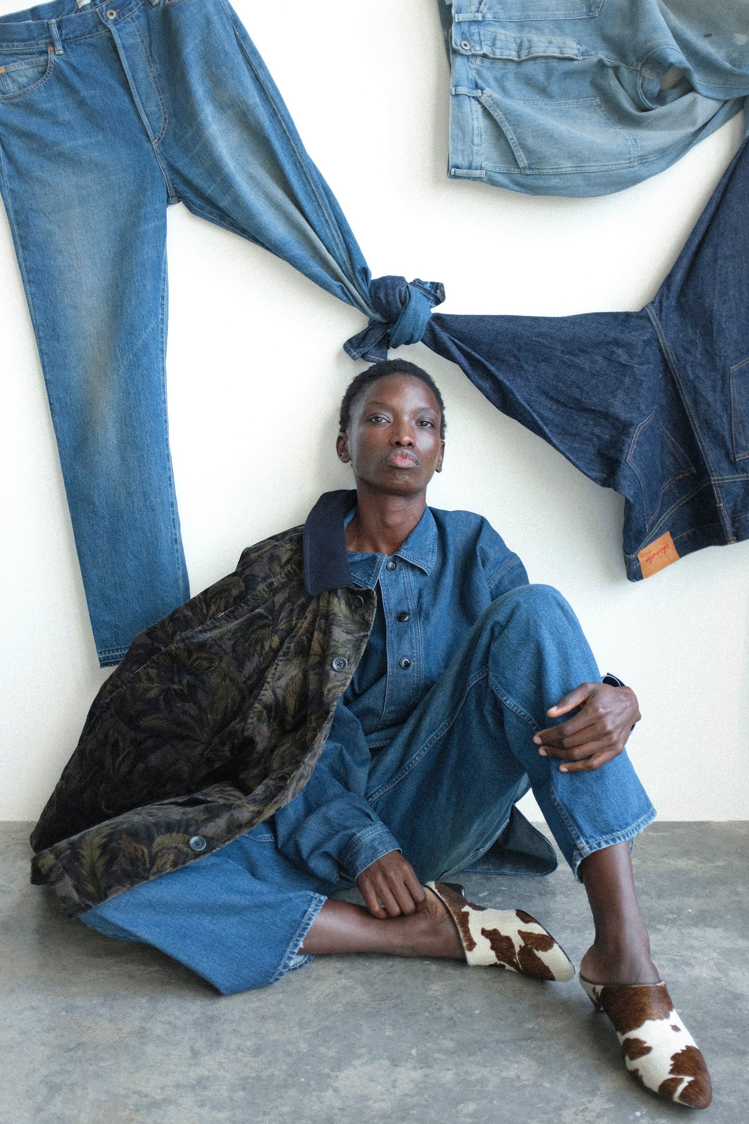 Person sitting on the floor surrounded by denim clothing and accessories.