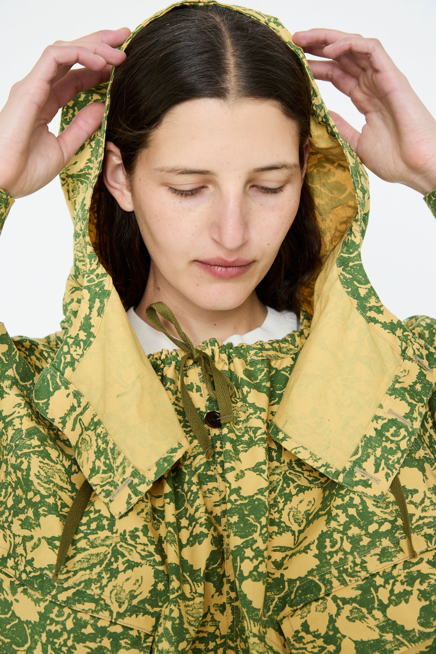 A person adjusts the Chimala Summer Leaf Smock Jacket in Camo, eyes closed, against a plain backdrop.