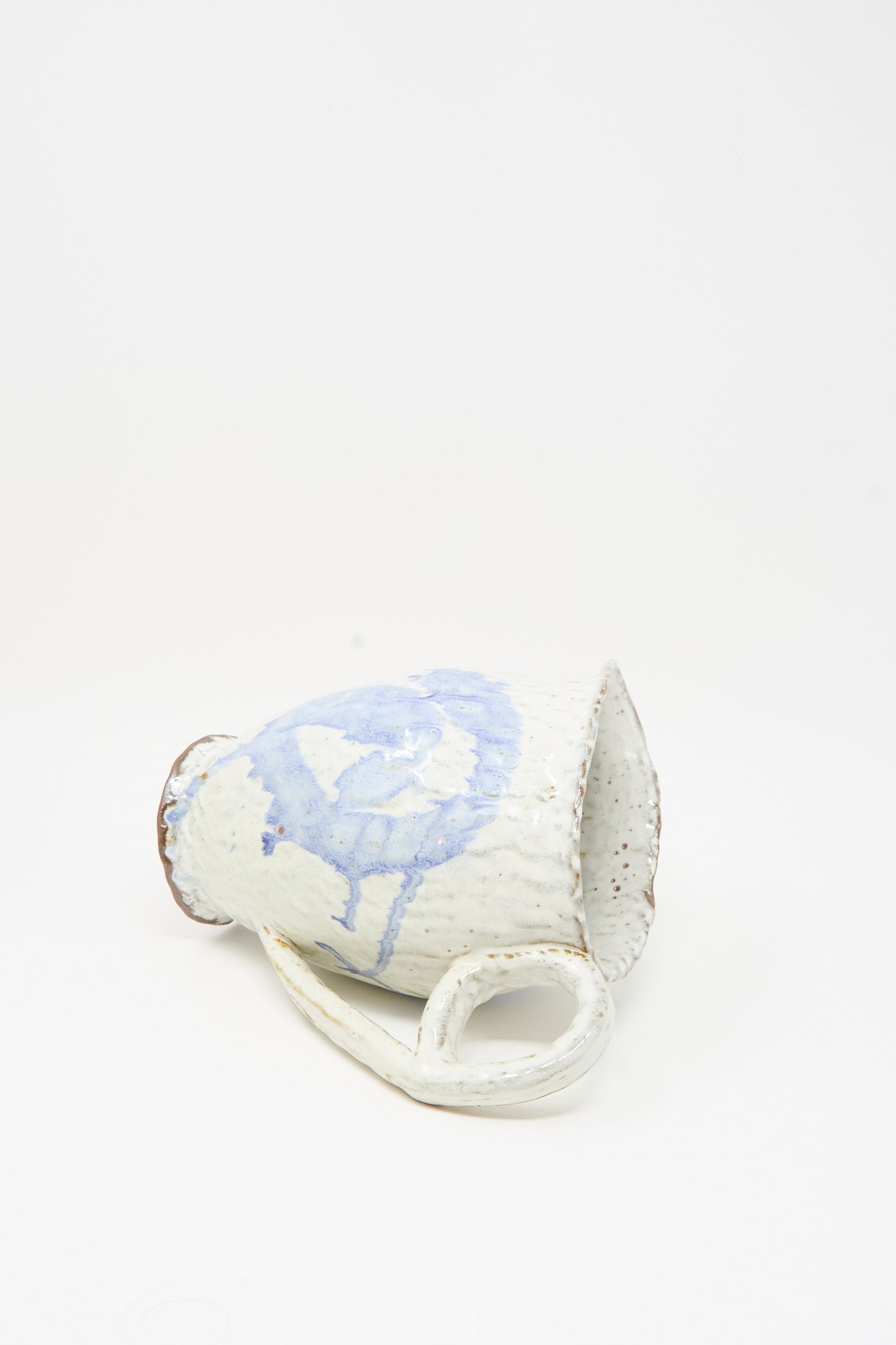 A handcrafted “Ceramic Pitcher in Blue” by Claire Resnick Ceramics, featuring a refined white and blue glaze, is shown resting on its side against a plain white background, highlighting the same elegant design found throughout Claire Resnick’s ceramic pieces.