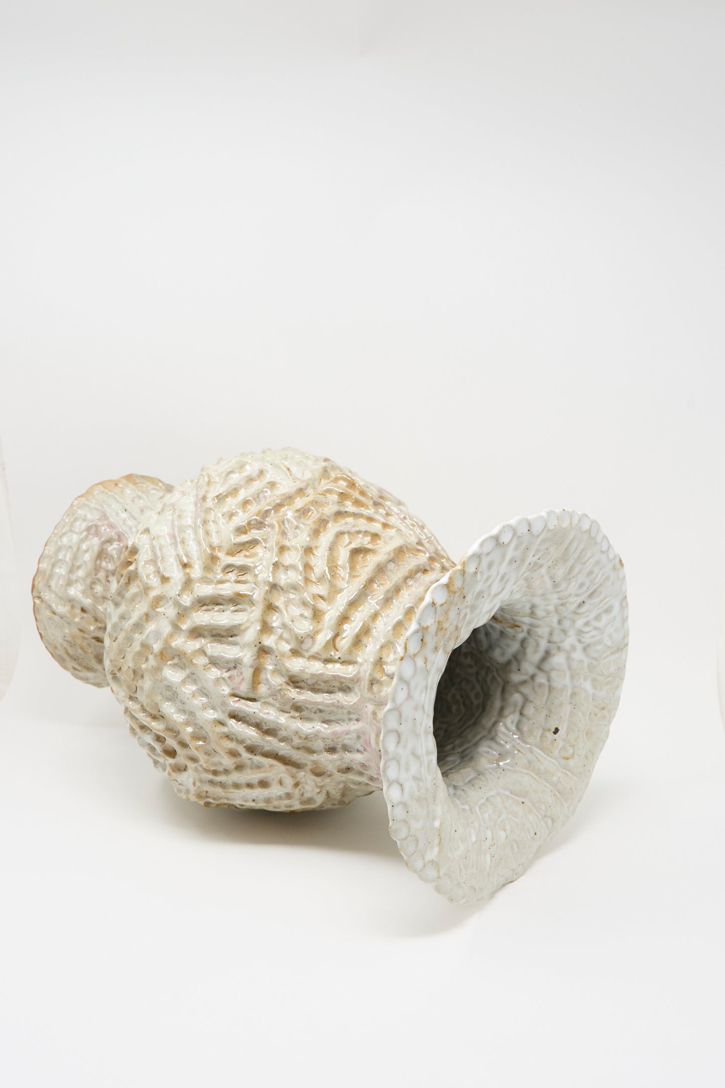 The Large Ridge Pedestal Vase in White by Claire Resnick Ceramics, featuring a textured ceramic surface and a wide, flared opening, is shown lying on its side against a plain white background.