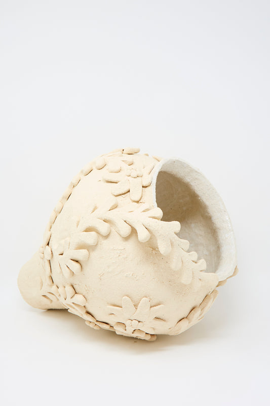 The Clandestine Le Jardin Enchanté Tall Amphora Vase, featuring textured beige ceramic with floral and leaf motifs, rests on its side against a plain white background.