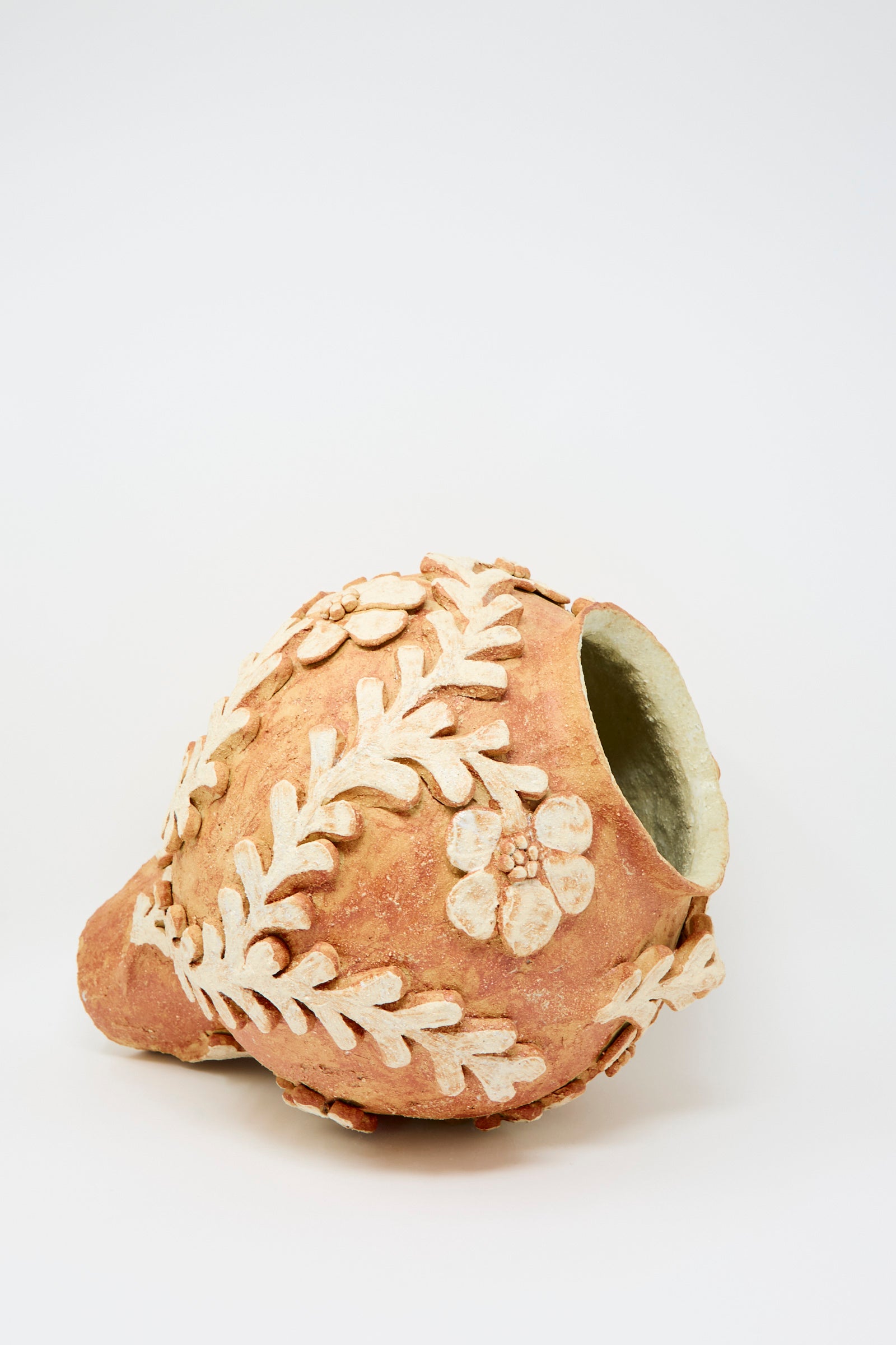The Le Jardin Secret Amphora Vase by Clandestine is handcrafted from sandy-textured clay with an irregular opening and raised floral motifs, showcased against a plain white background.