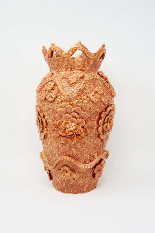 The Le Jardin Vase in Rust by Clandestine features ornate raised floral motifs and a crown-like rim with a speckled orange and gold glaze, displayed against a plain white background.
