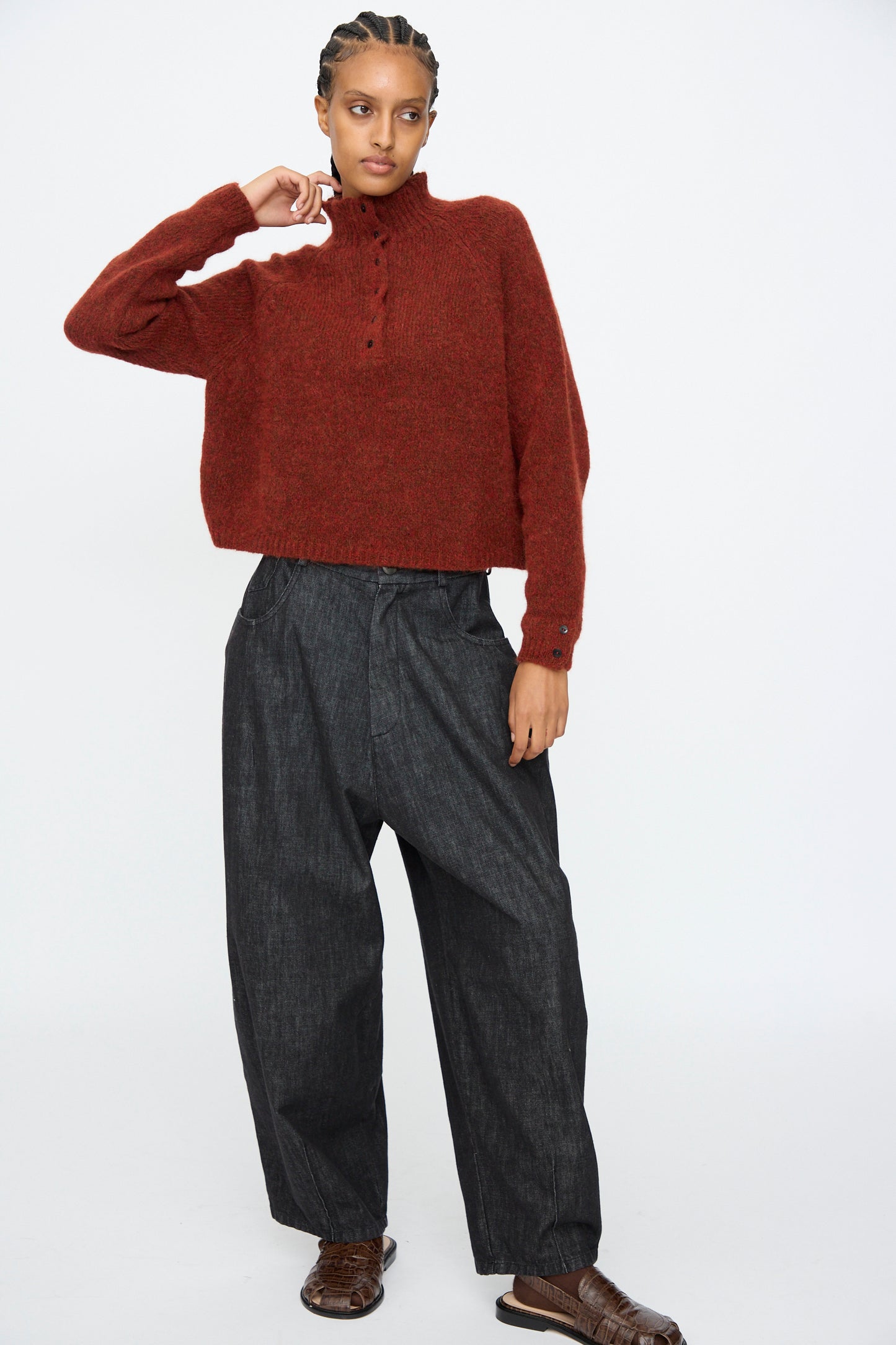 A person wears the Cordera Baby Alpaca Polo Sweater in Terracotta, paired with loose dark denim pants and brown shoes, standing against a plain white background.