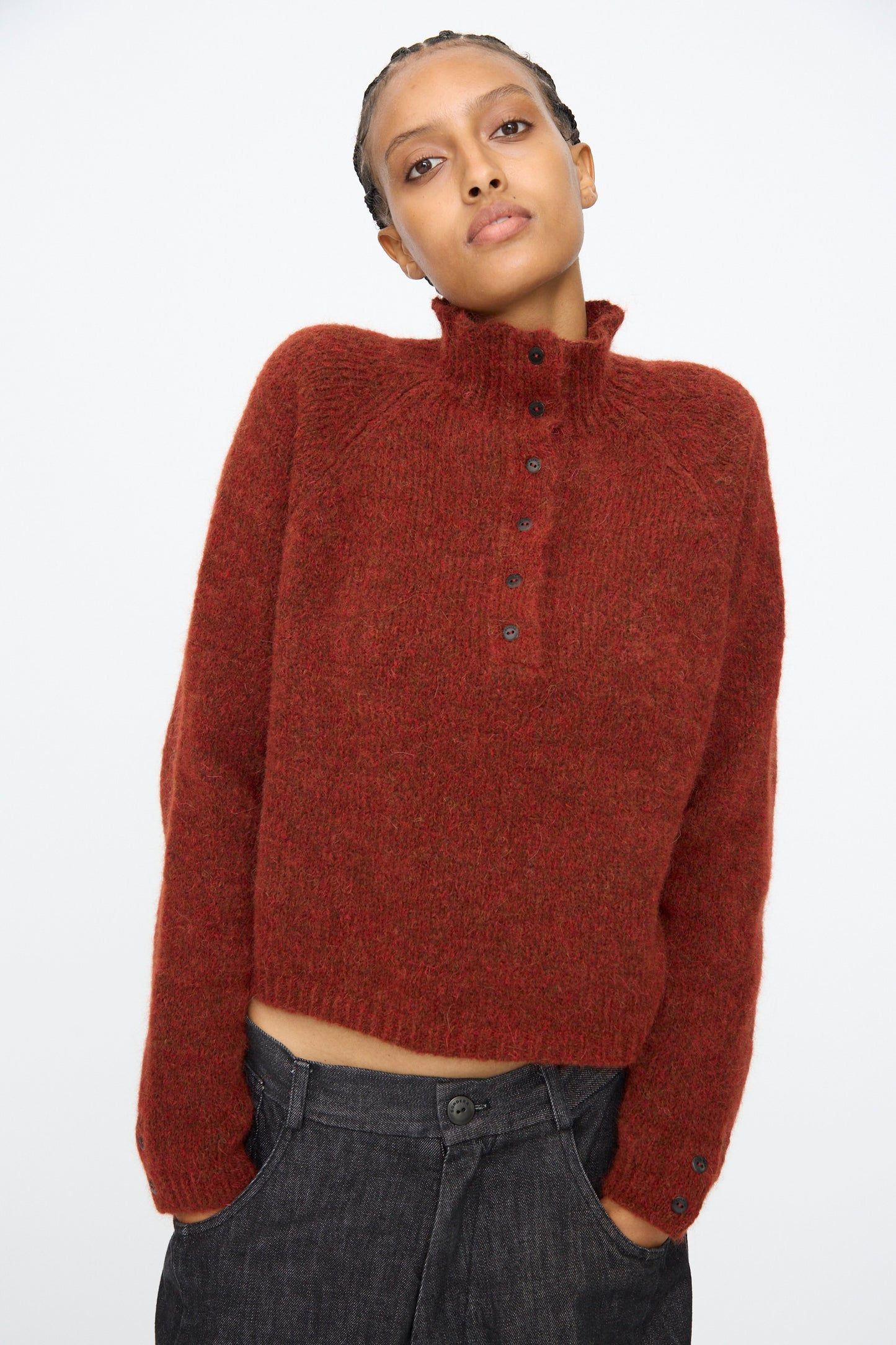 A person wears the Cordera Baby Alpaca Polo Sweater in Terracotta, featuring a textured knit and buttoned collar, paired with loose dark pants, standing against a plain background.