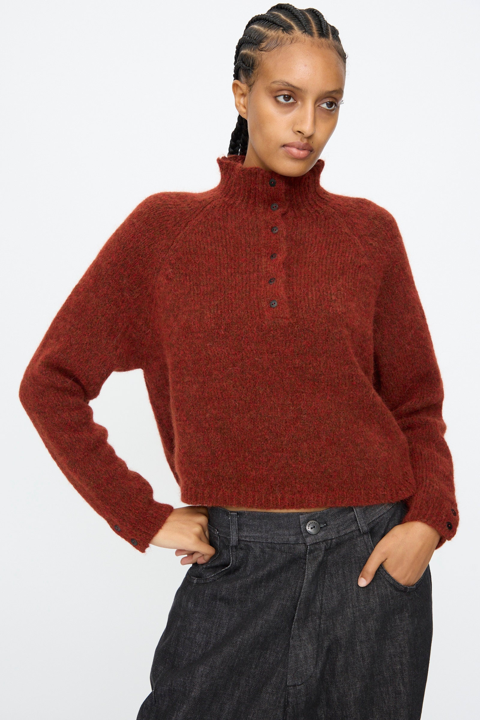 A person wearing the Cordera Baby Alpaca Polo Sweater in Terracotta and dark gray pants stands with one hand in their pocket against a plain white background.
