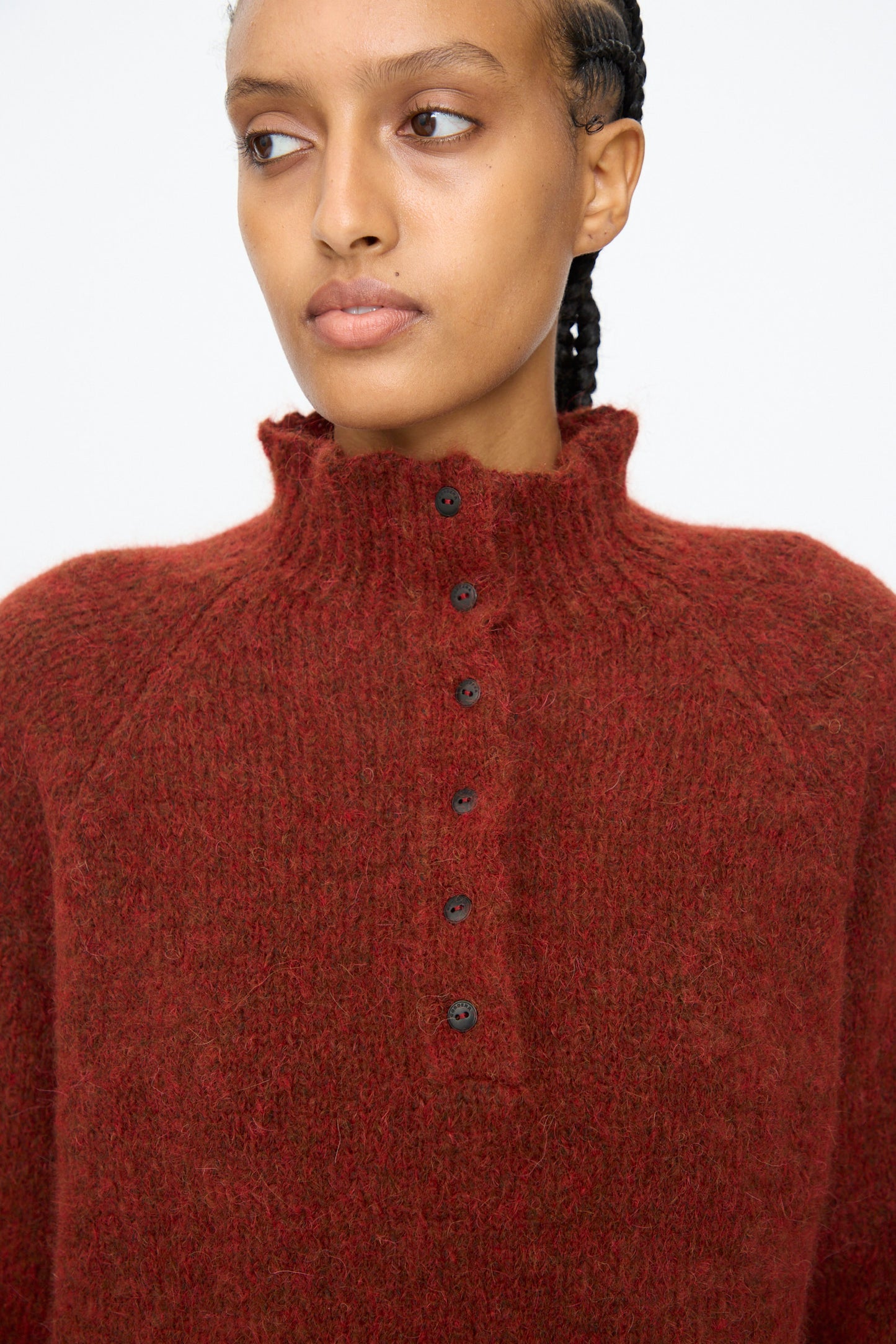 A person wears the Cordera Baby Alpaca Polo Sweater in terracotta, featuring a high neck and button placket, while looking slightly to the side against a plain background.