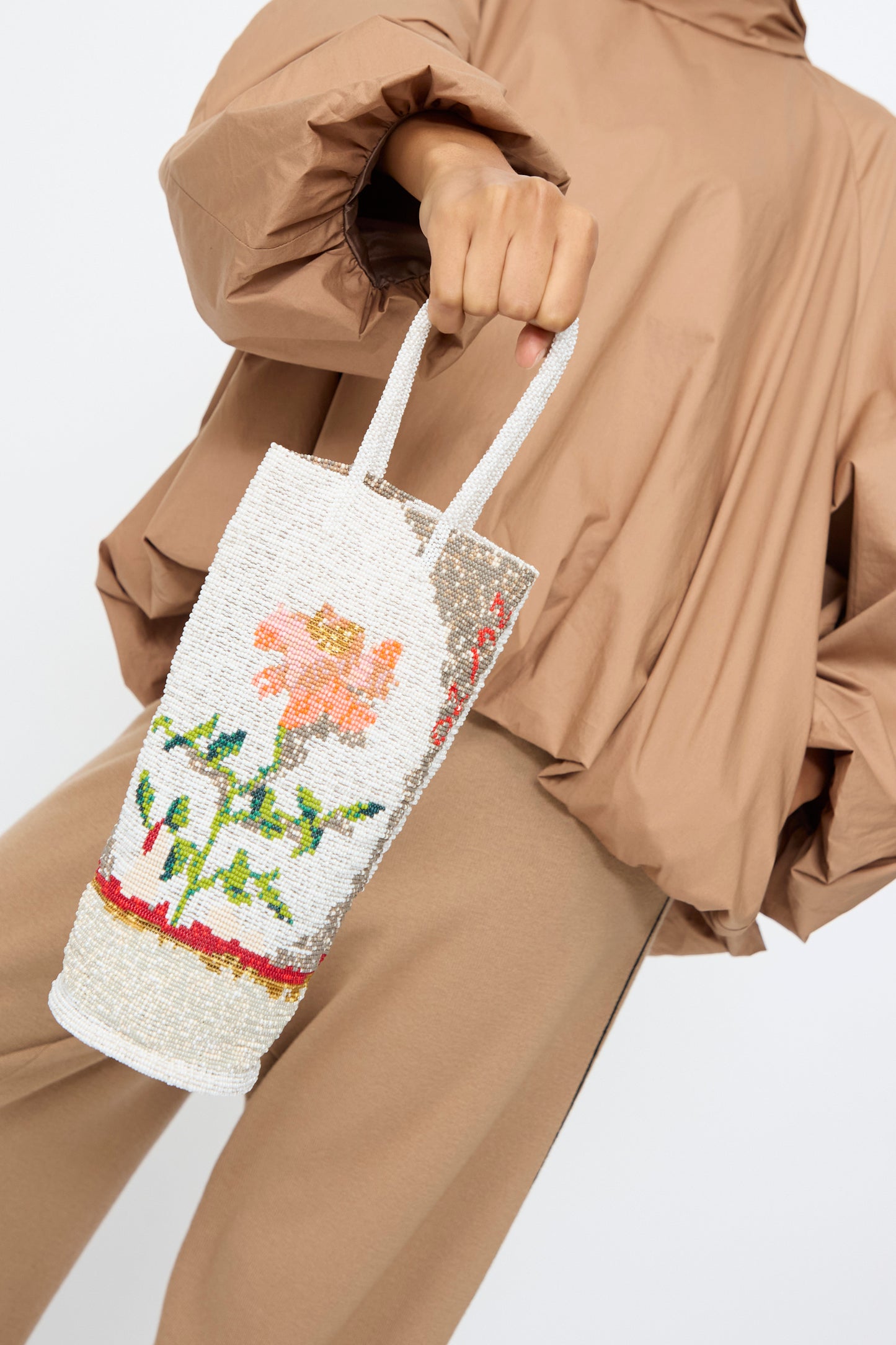 A person in tan clothing holds the Cordera Beaded Bag in Fiore, a handcrafted accessory from Guatemala with floral designs and two handles.