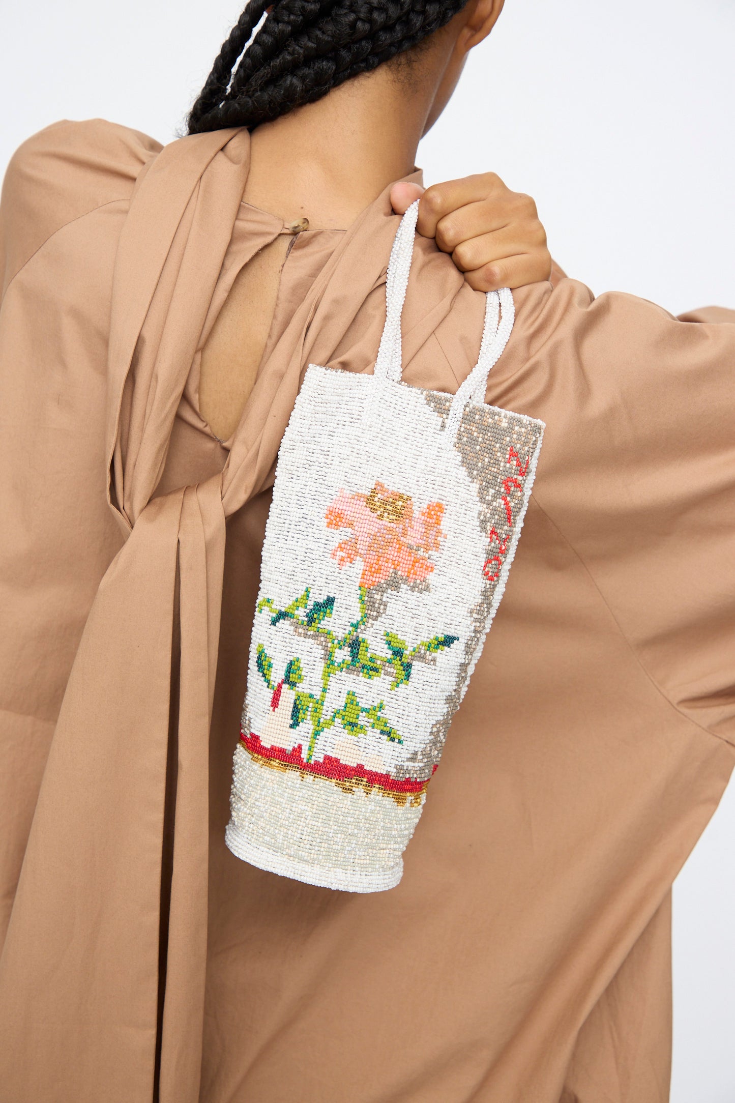 A person holds Cordera’s Beaded Bag in Fiore, featuring a handcrafted floral design. Wearing a loose tan garment tied at the back, only their hand and back are shown—highlighting artistry inspired by Guatemalan traditions.
