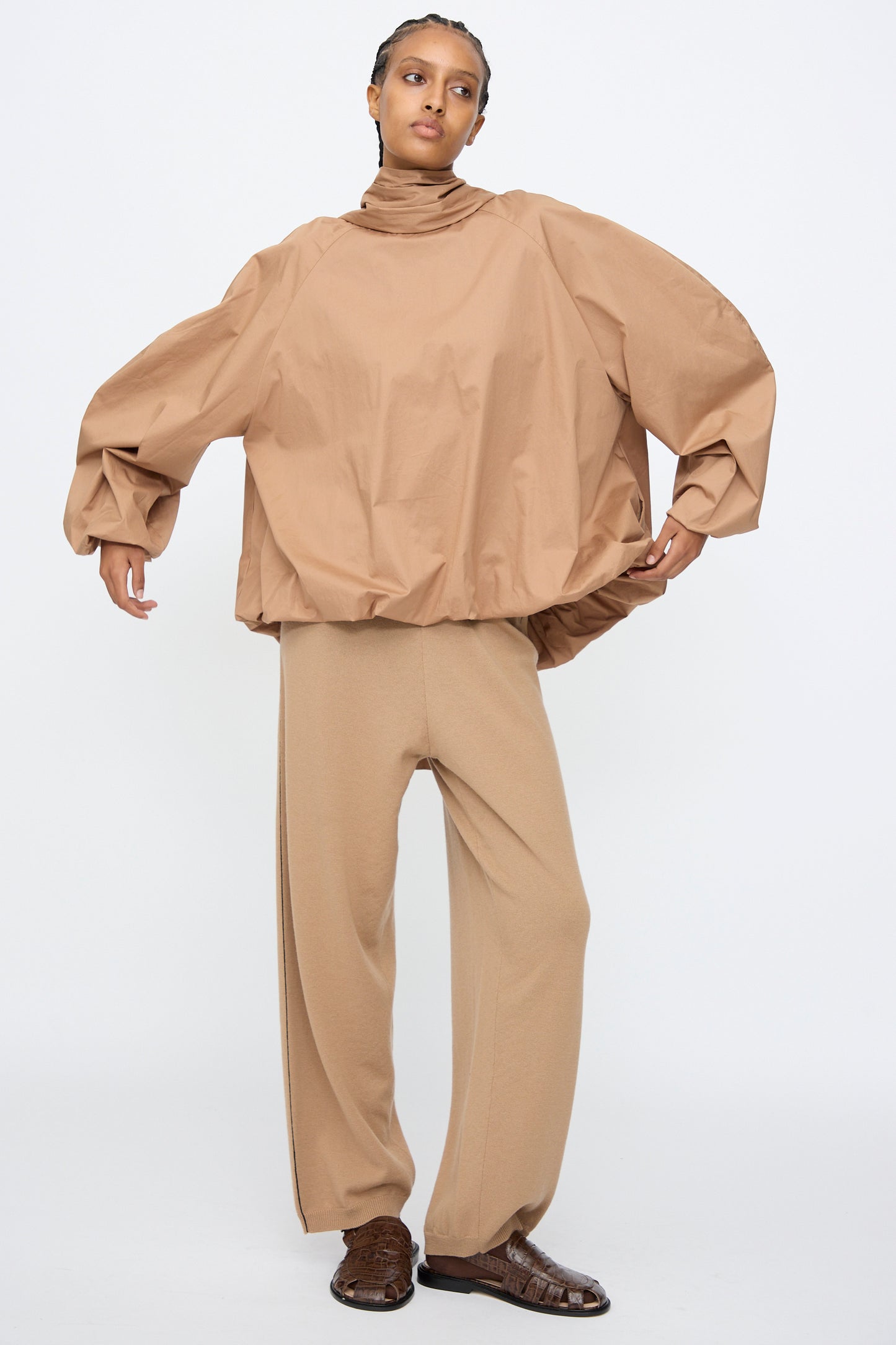 A person models the Cordera Bow Shirt in Camel—a loose cotton-blend balloon-silhouette top with voluminous sleeves—paired with matching wide-leg pants and brown shoes, standing against a plain white background.