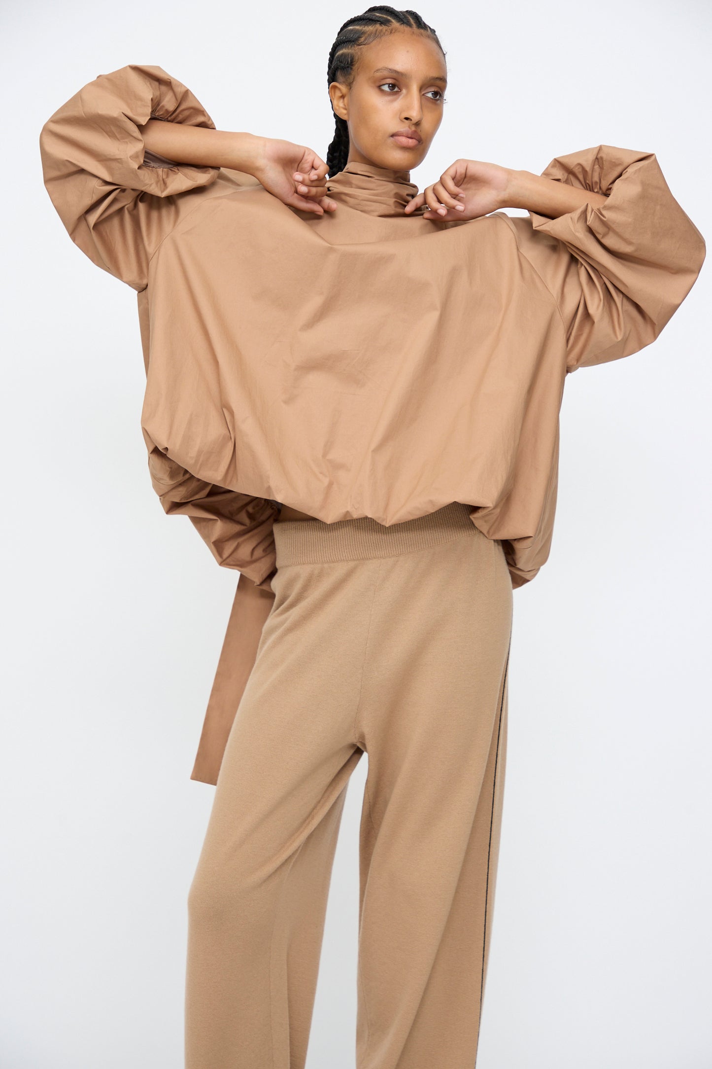 A person stands against a plain background wearing the Cordera Bow Shirt in Camel, featuring a loose balloon silhouette with voluminous sleeves, paired with matching wide-leg pants.