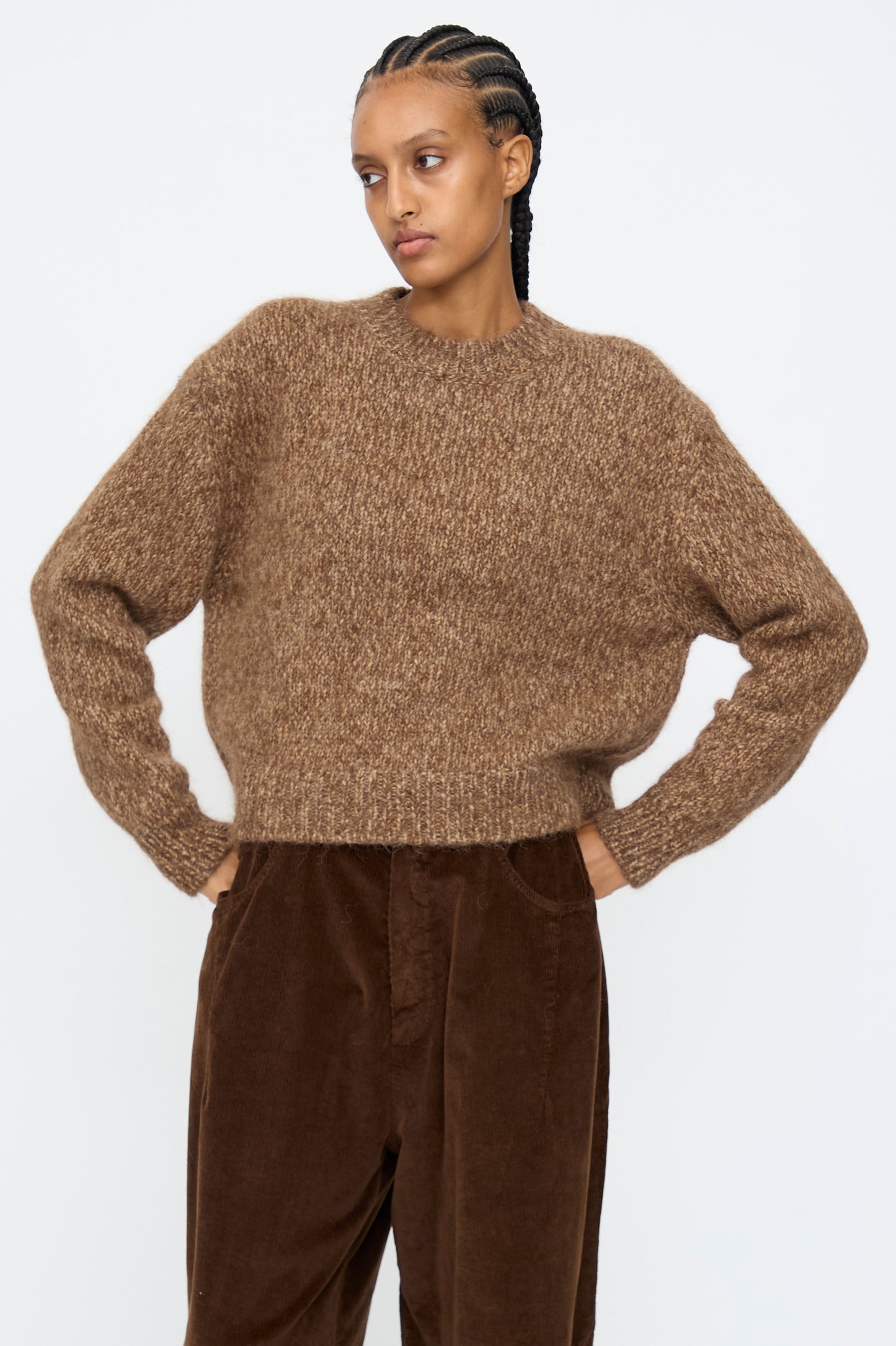 A person wearing the Cordera Chunky Sweater in Brown Melange stands against a plain white background with their hands on their hips.