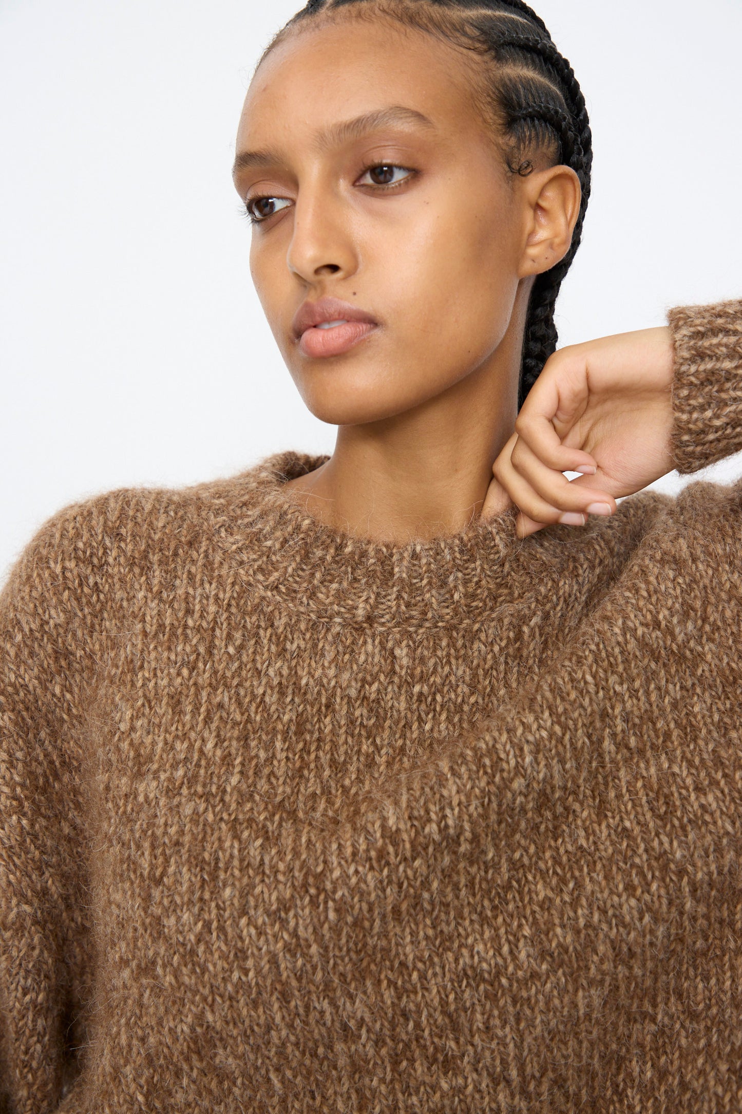 A person with braided hair wears the Cordera Chunky Sweater in Brown Melange, looking slightly to the side with a neutral expression.