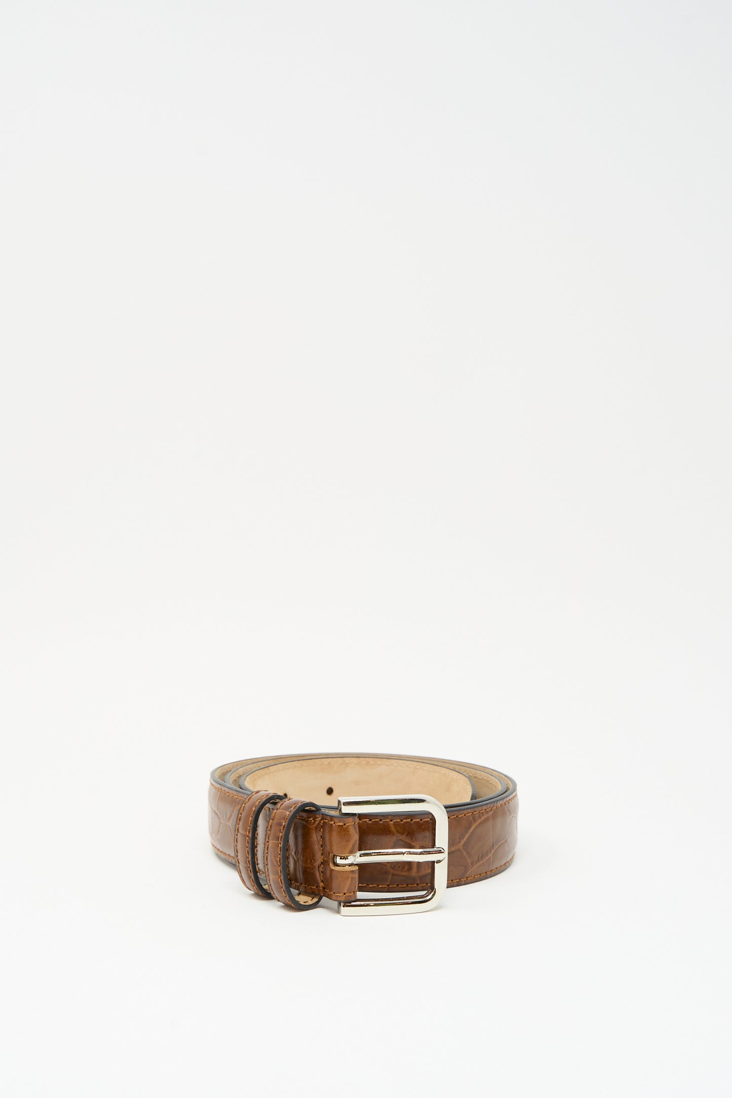 The Classic Belt in Caramel Crocodile by Cordera, featuring crocodile-printed calfskin leather and a silver buckle, is coiled upright on a plain white background.