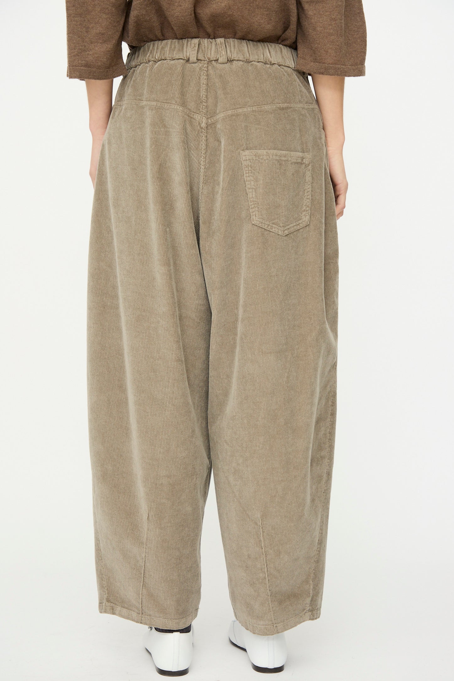 A person is seen from the back wearing Cordera’s Corduroy Baggy Pant in Cobblestone, made in Spain. The light brown pants feature an elastic waistband and a single back pocket for a relaxed, comfortable look.